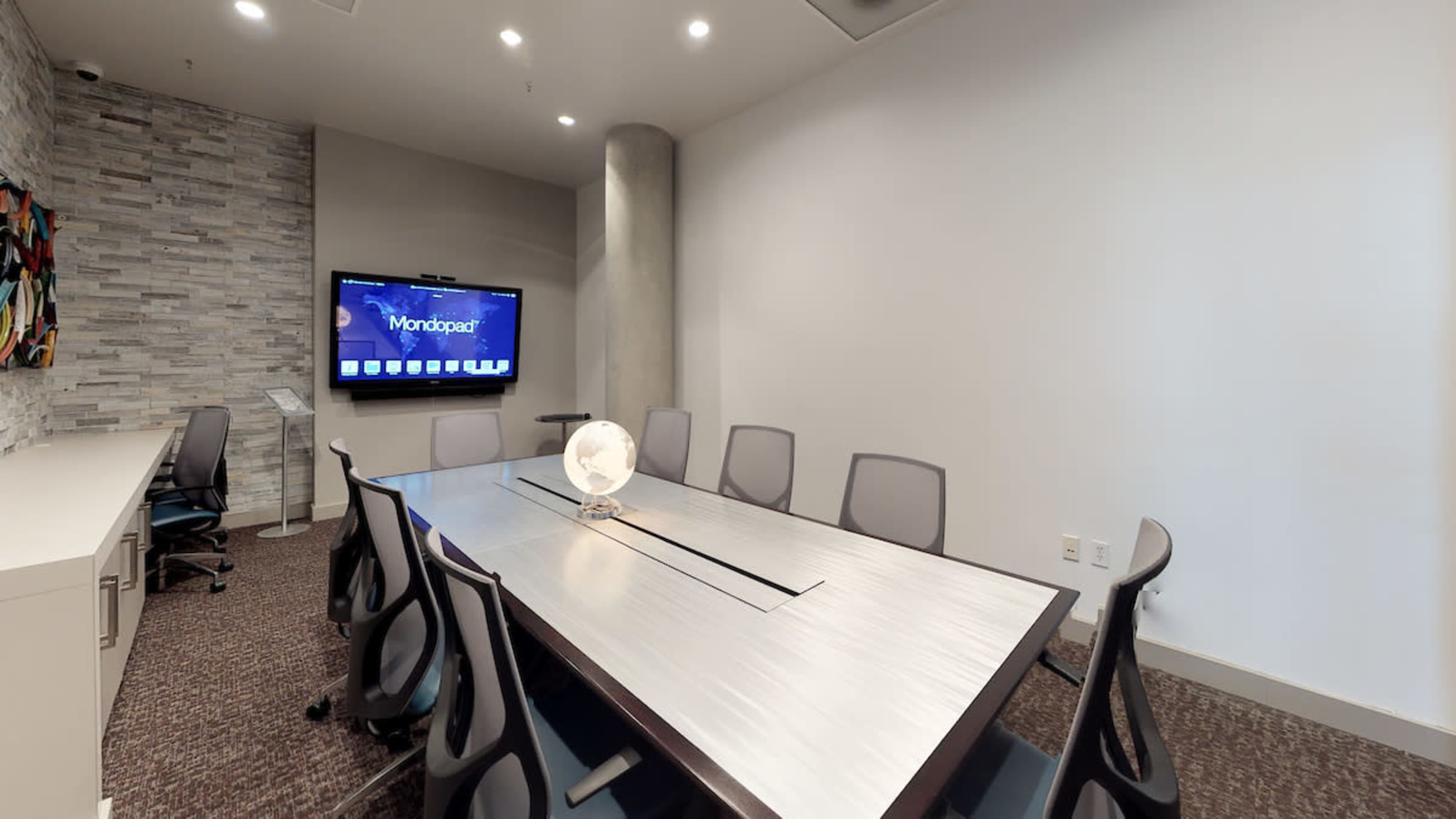 A modern conference room with a long table, several chairs, a television screen on the wall, and a decorative globe in the center.