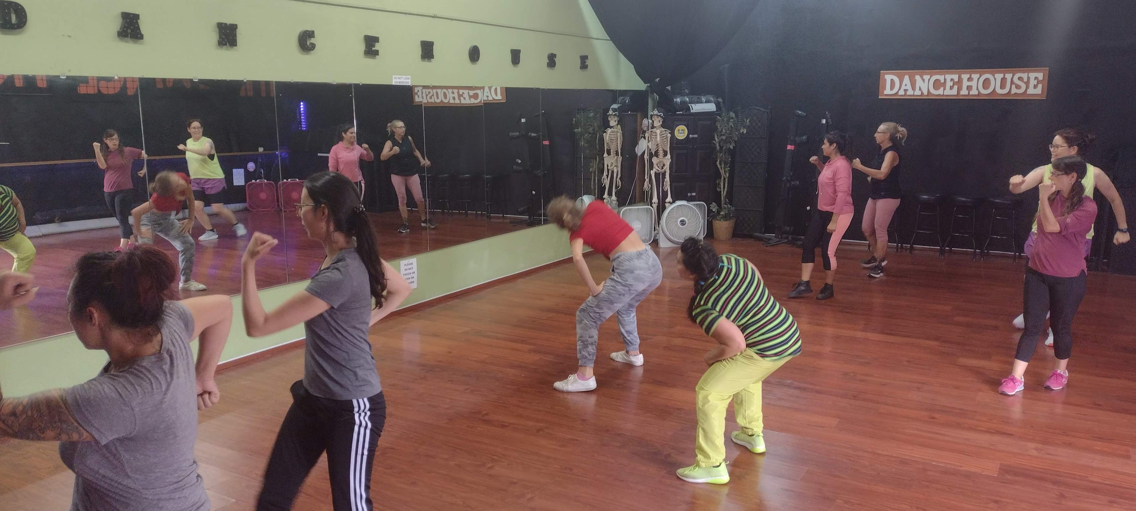 A group of individuals is participating in a dance class inside a studio with mirrors and a wooden floor.