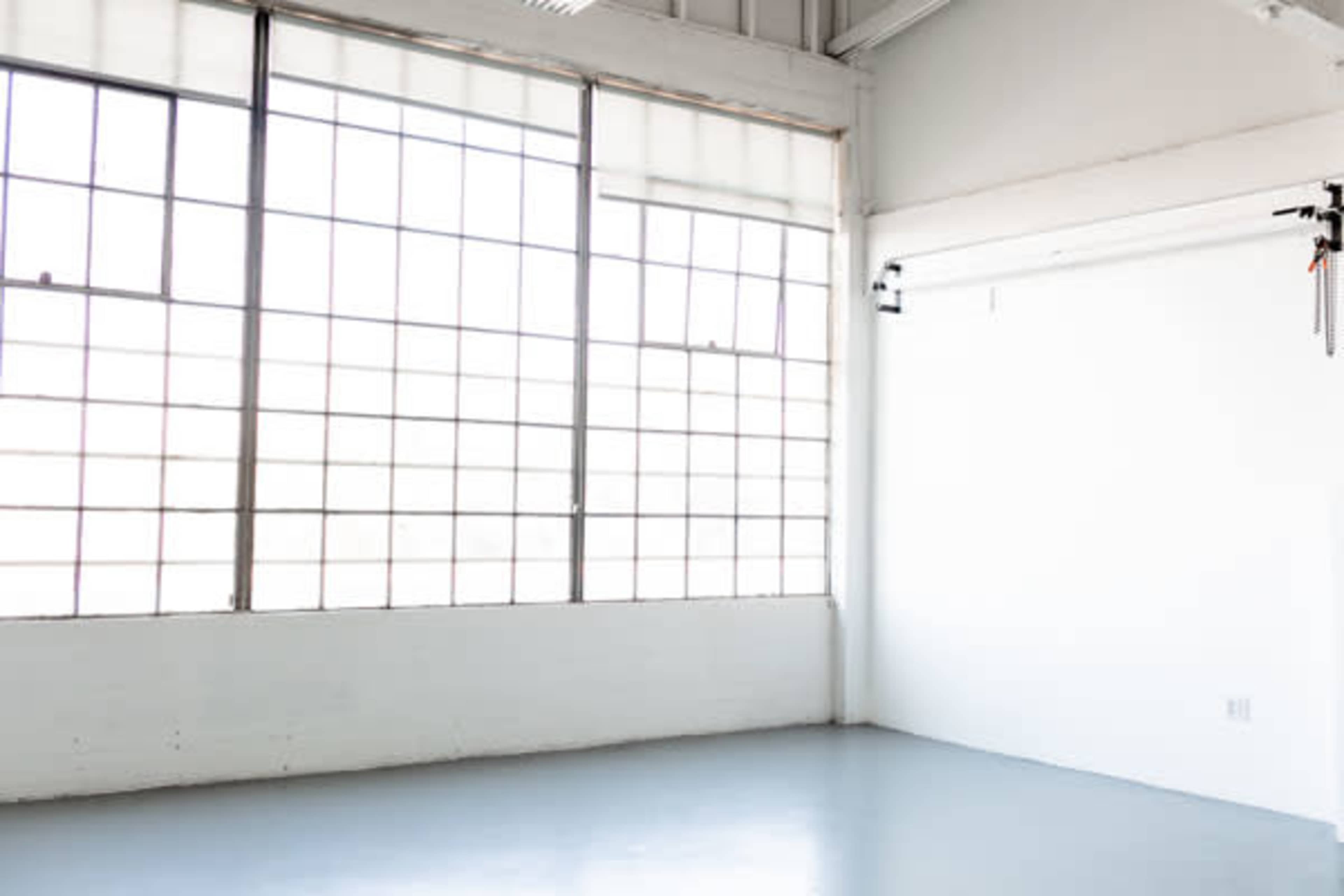 A bright, empty studio space with large windows and a blank white wall.