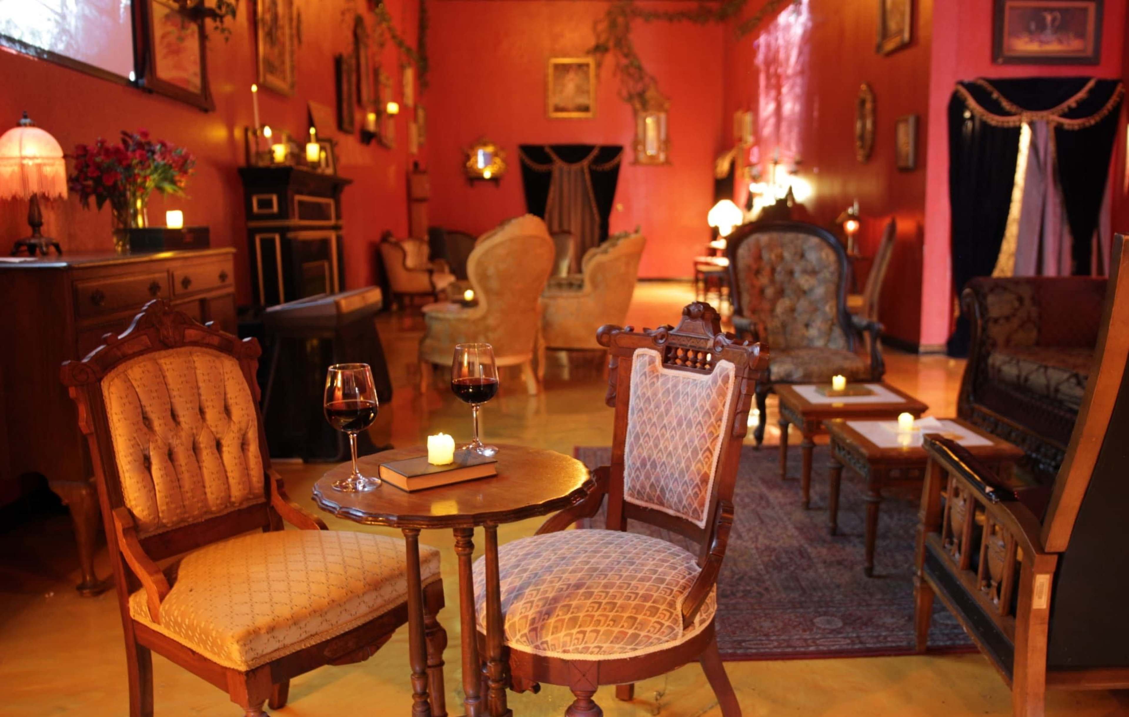 The scene depicts a cozy interior of a vintage-style lounge with vintage furniture, dim lighting, and two glasses of red wine on a small table.