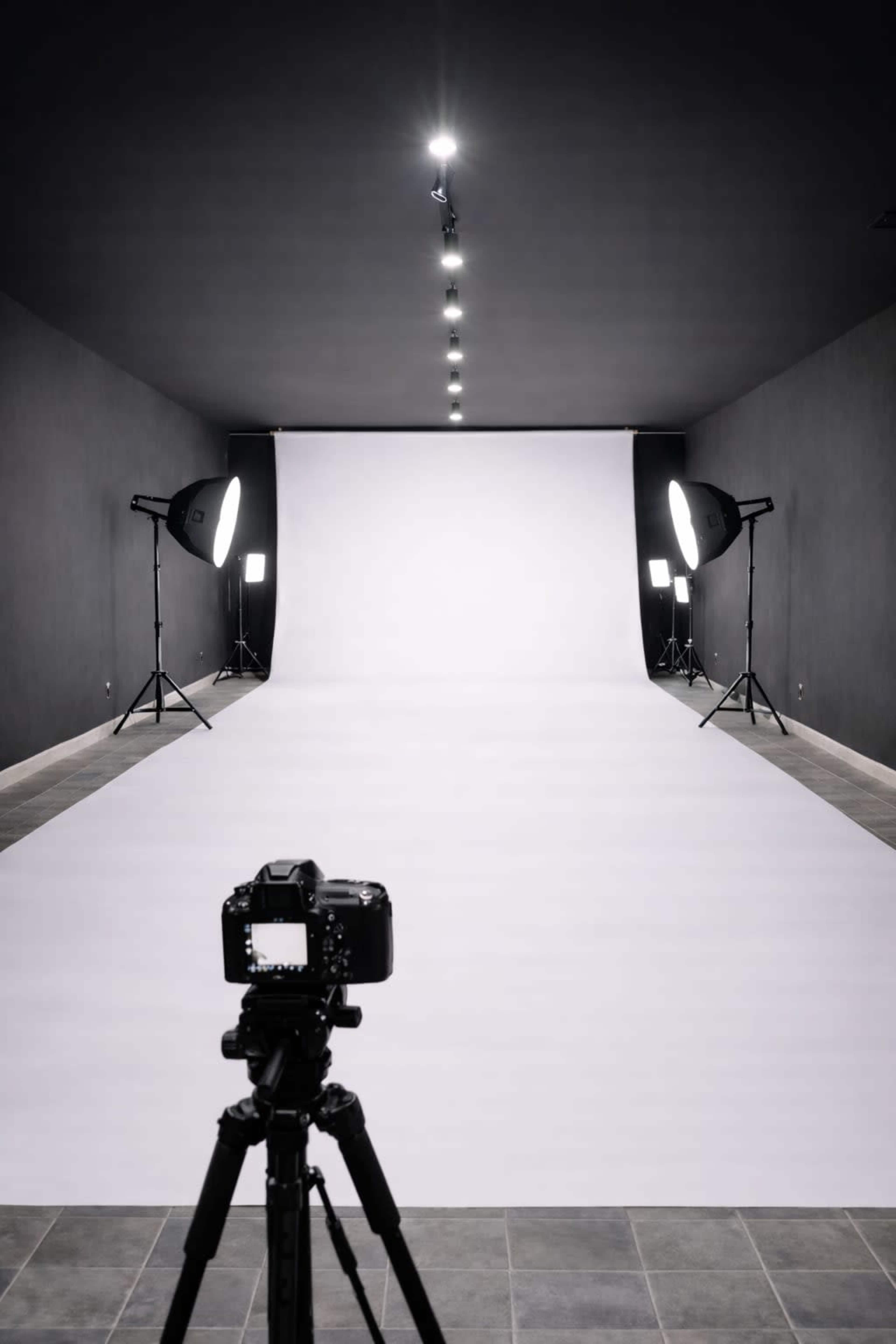 A photography studio features a camera positioned in front of a seamless white backdrop, with studios lights set up on either side.