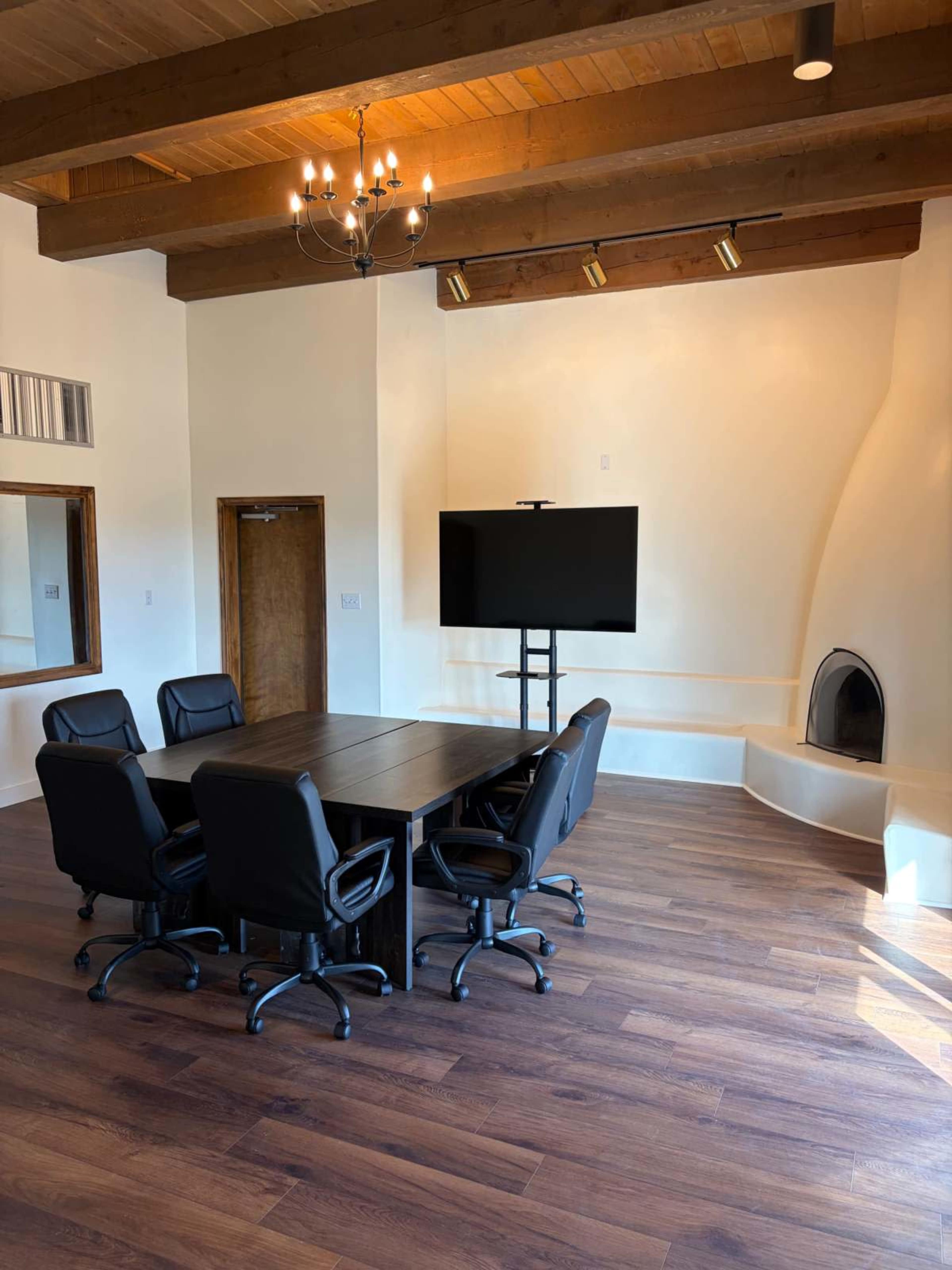 The image shows a modern conference room with a large table surrounded by black office chairs, a flat-screen TV on a stand, and an architectural feature in the corner resembling a fireplace.