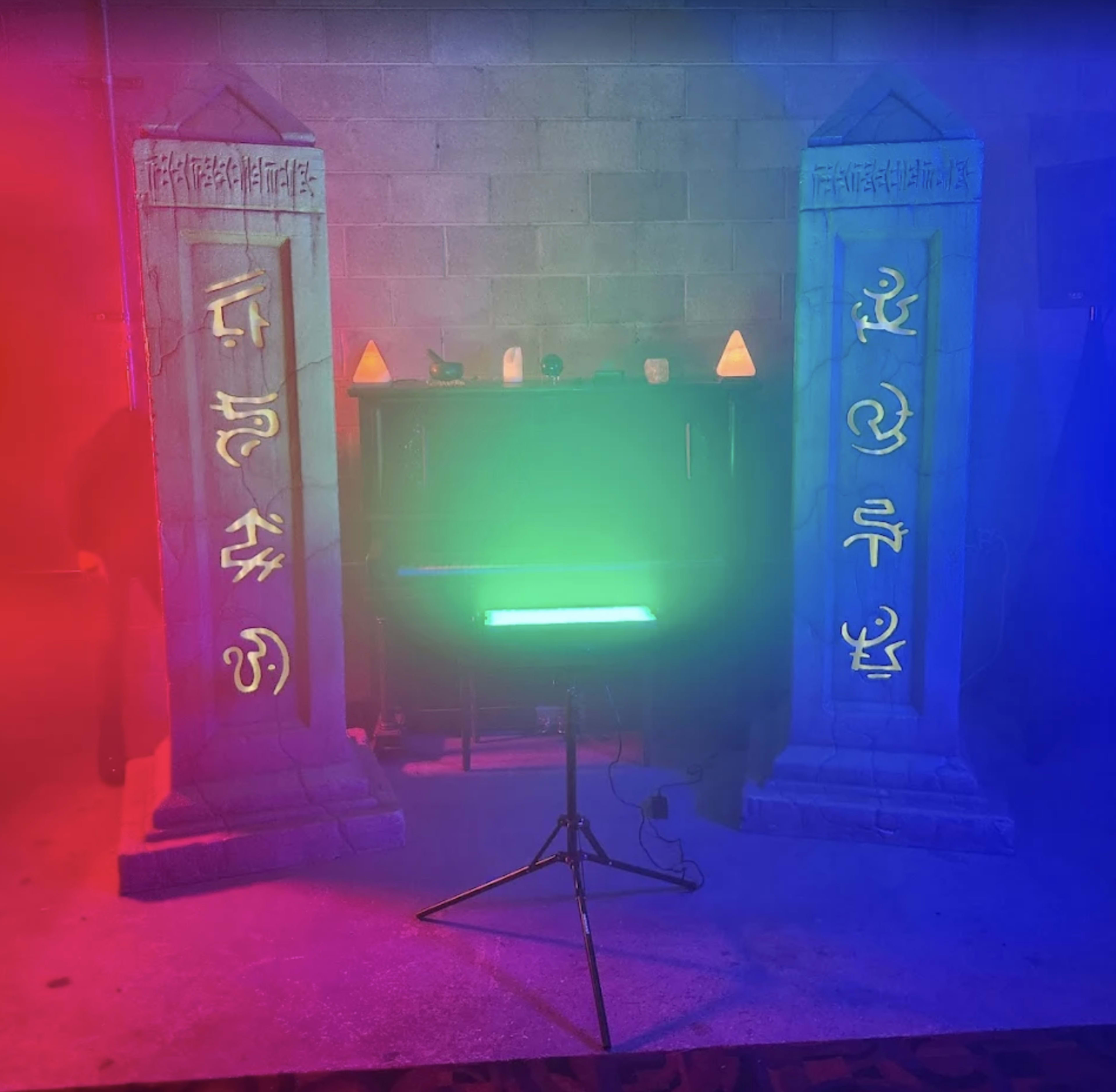 The scene features two stone pillars illuminated with red and blue lighting, standing on either side of a backdrop that includes a table with decorative objects.