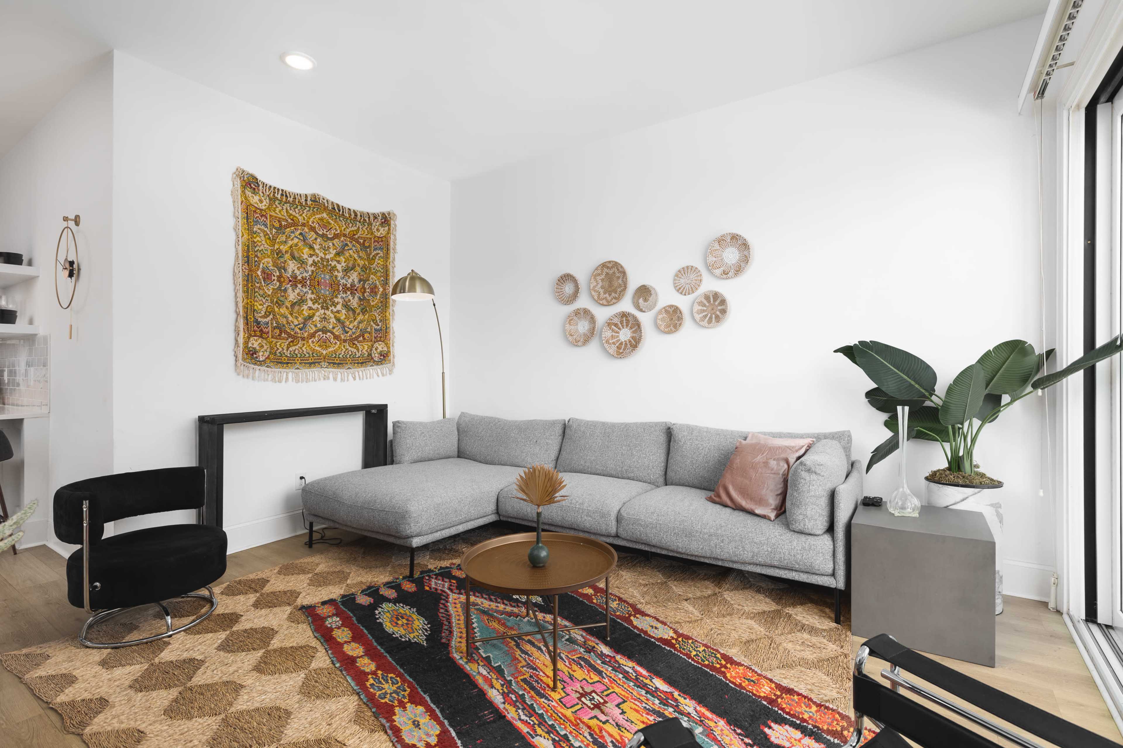 A modern living room featuring a gray sectional sofa, a round coffee table, decorative wall art, and lush indoor plants.