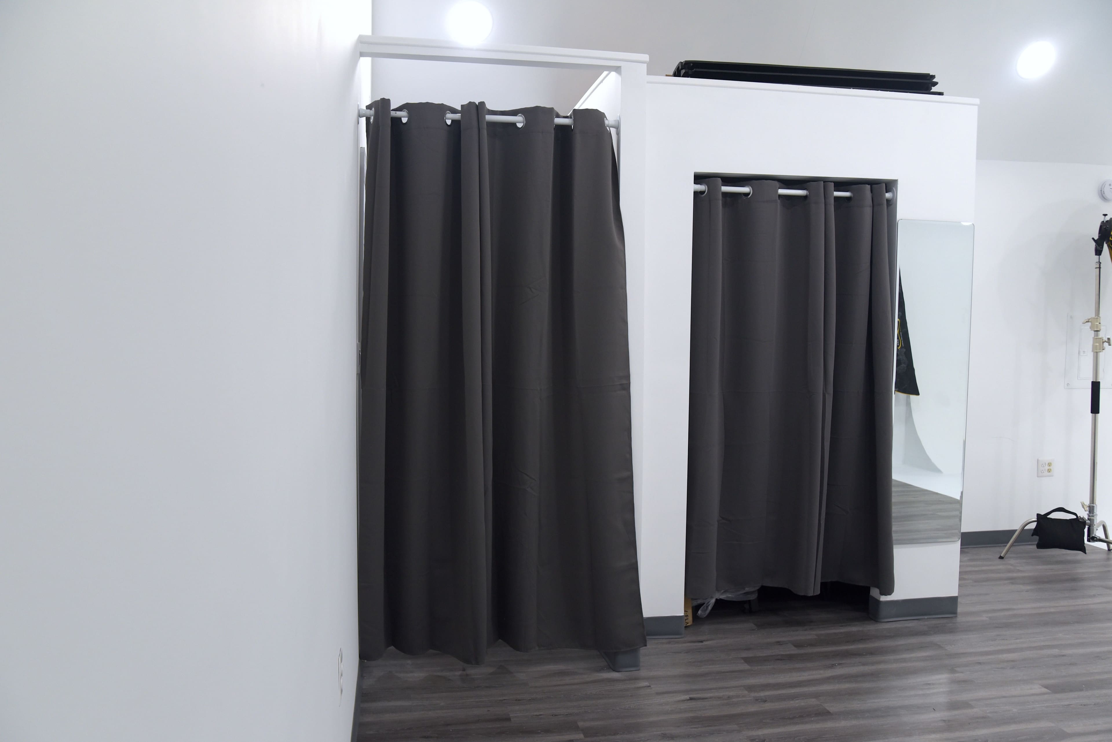 A spacious room with dark fabric curtains dividing two dressing areas, along with a mirror and light setup in the background.