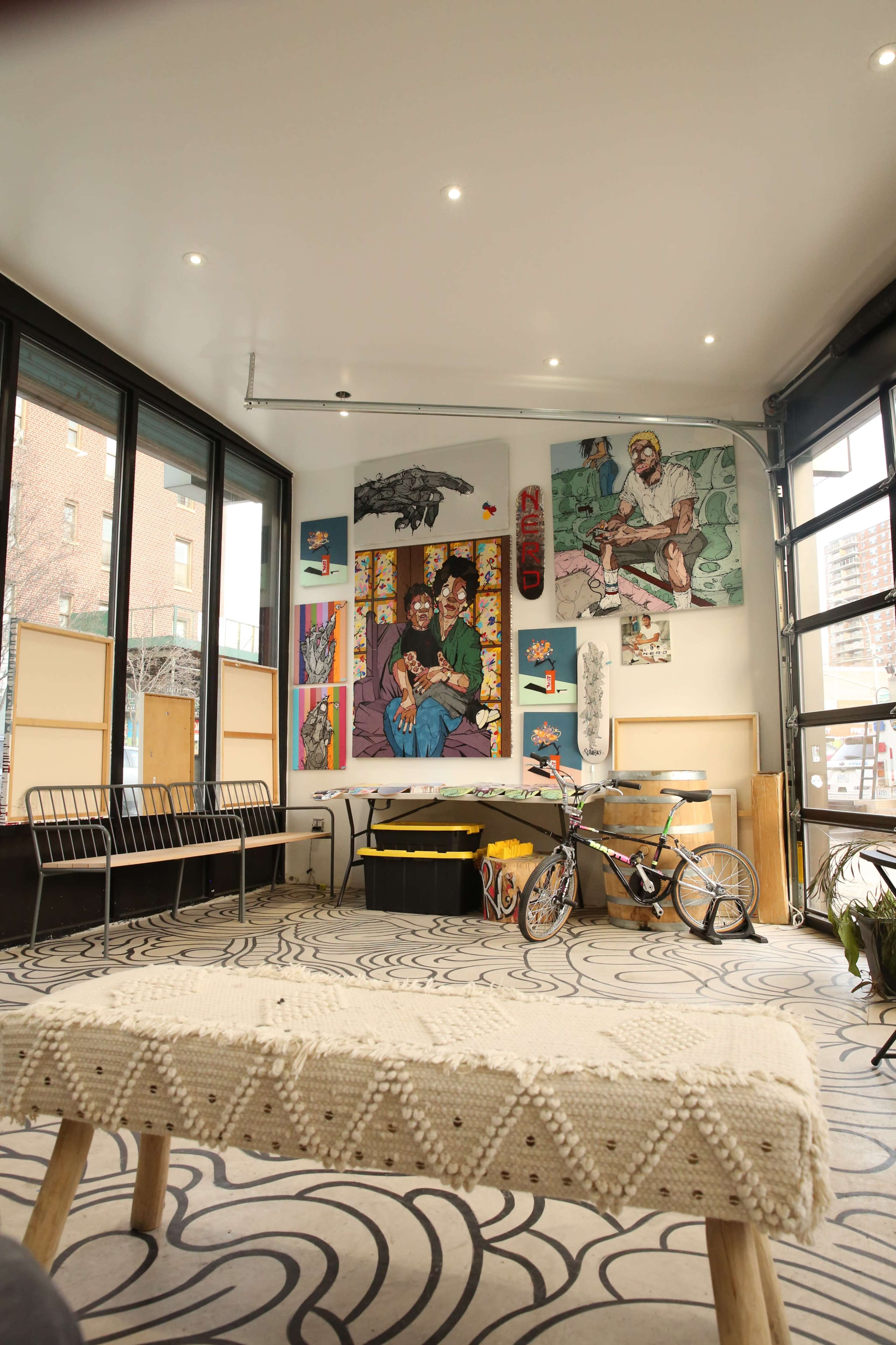 A modern interior space with a patterned floor, a bicycle, artwork on the walls, and a wooden table in the center.