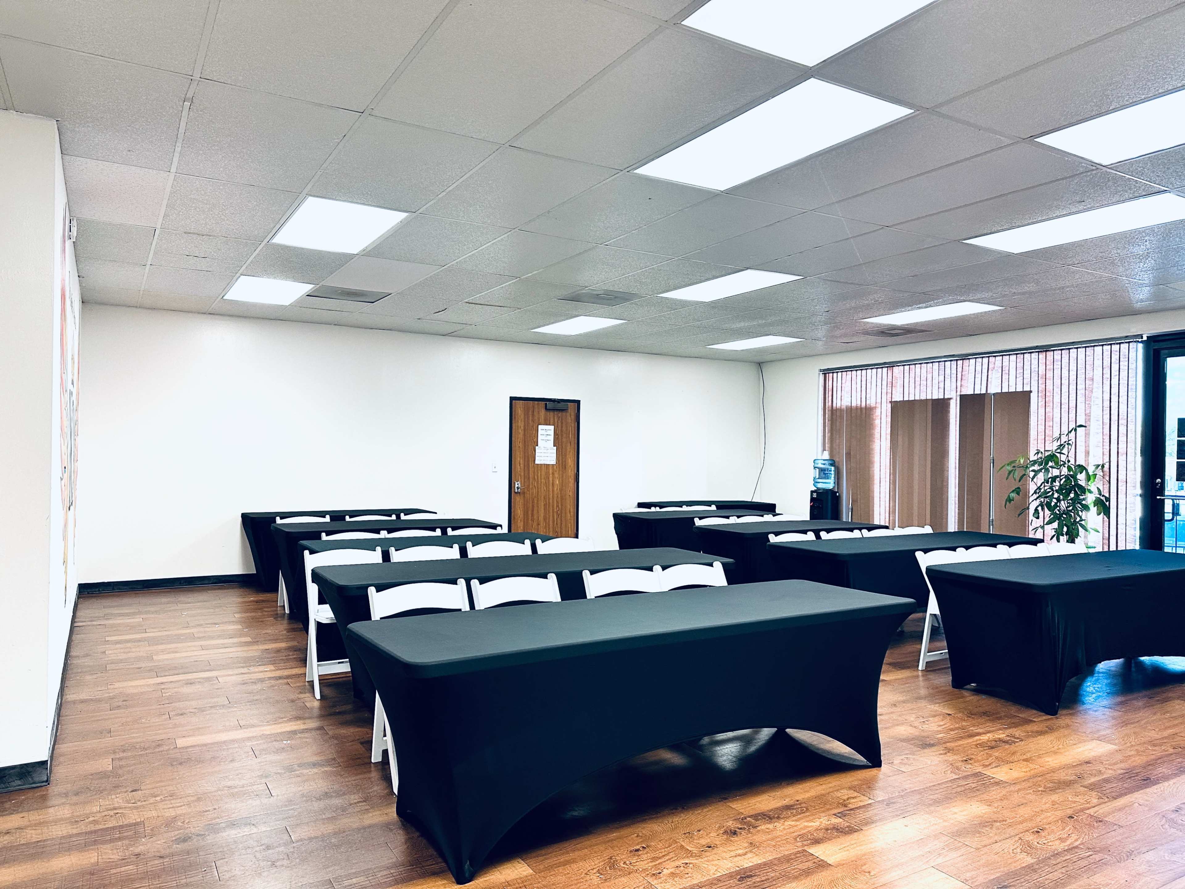A spacious room features several neatly arranged tables covered in black tablecloths, with a few chairs positioned around them.