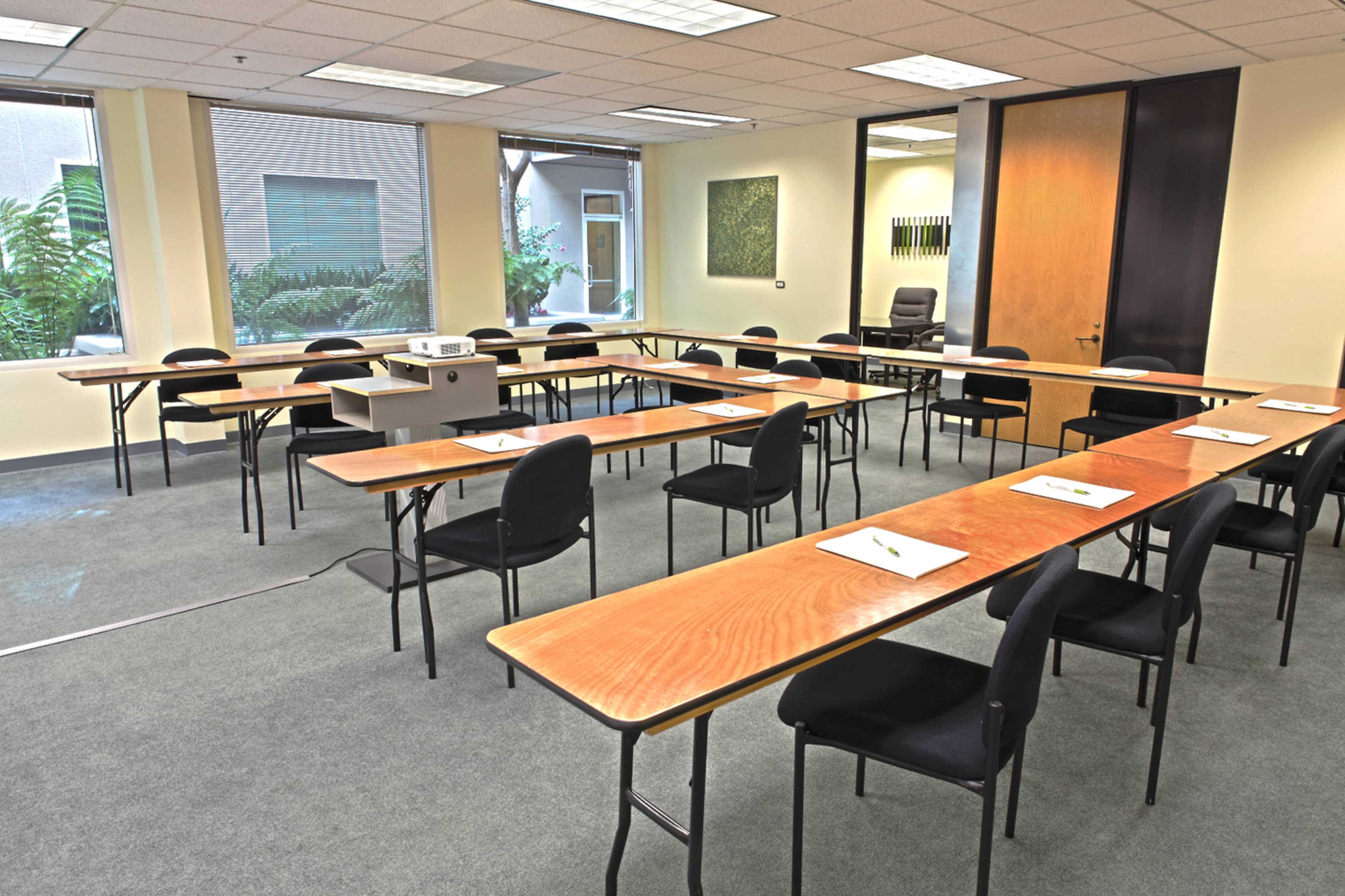 A classroom or meeting room arranged with multiple tables and chairs, equipped with a projector at the front.