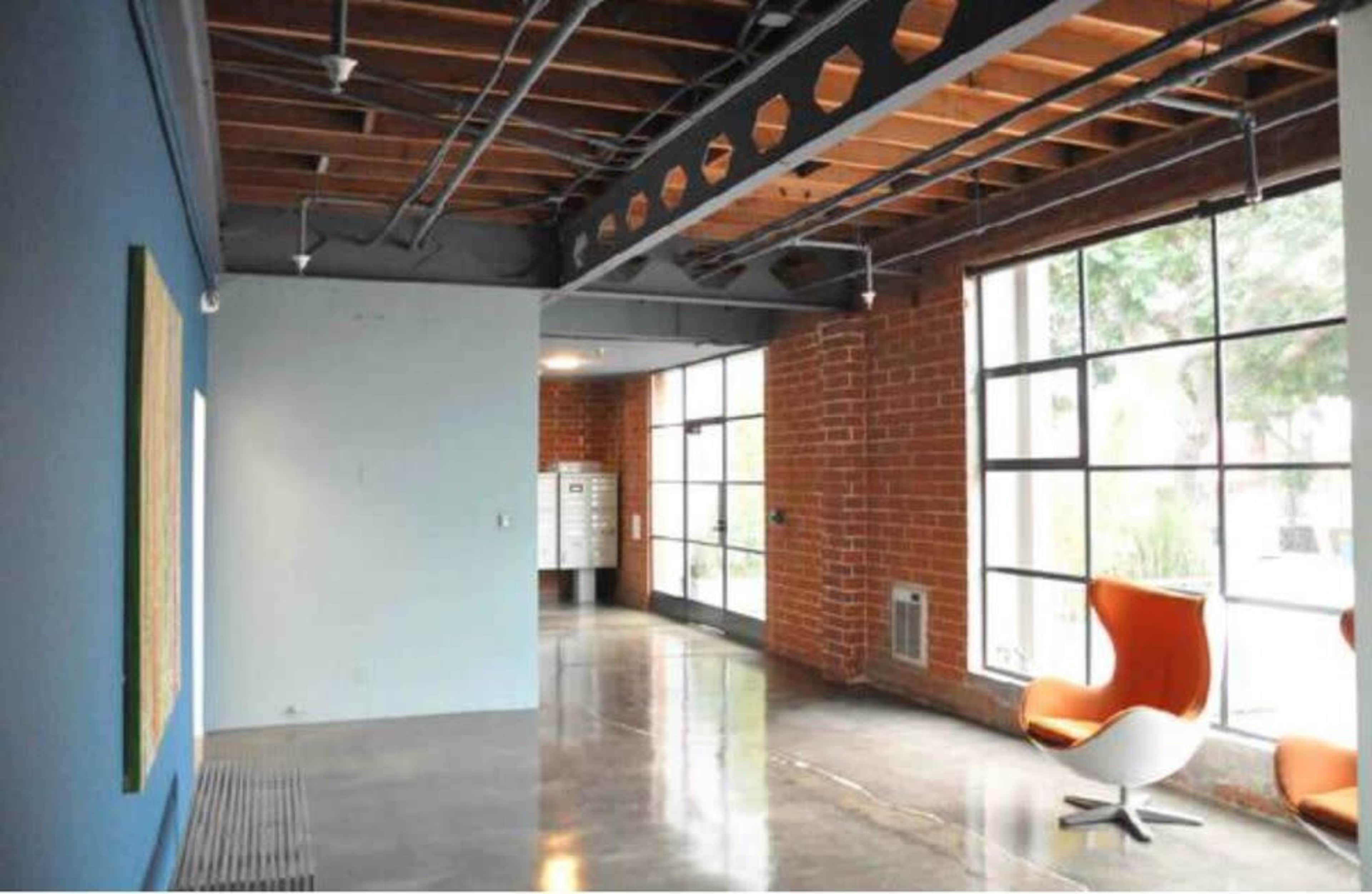 The image shows a modern interior space with exposed brick walls, large windows, and a bright orange chair.
