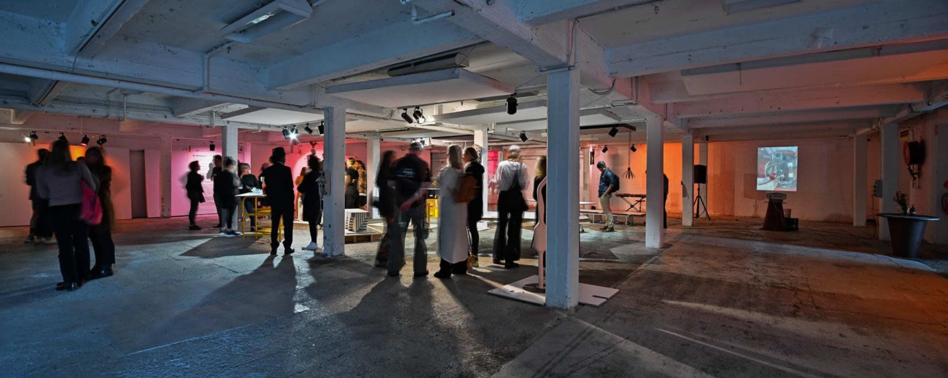 A crowd of people mingles in a spacious, dimly lit gallery featuring artworks and illuminated wall installations.