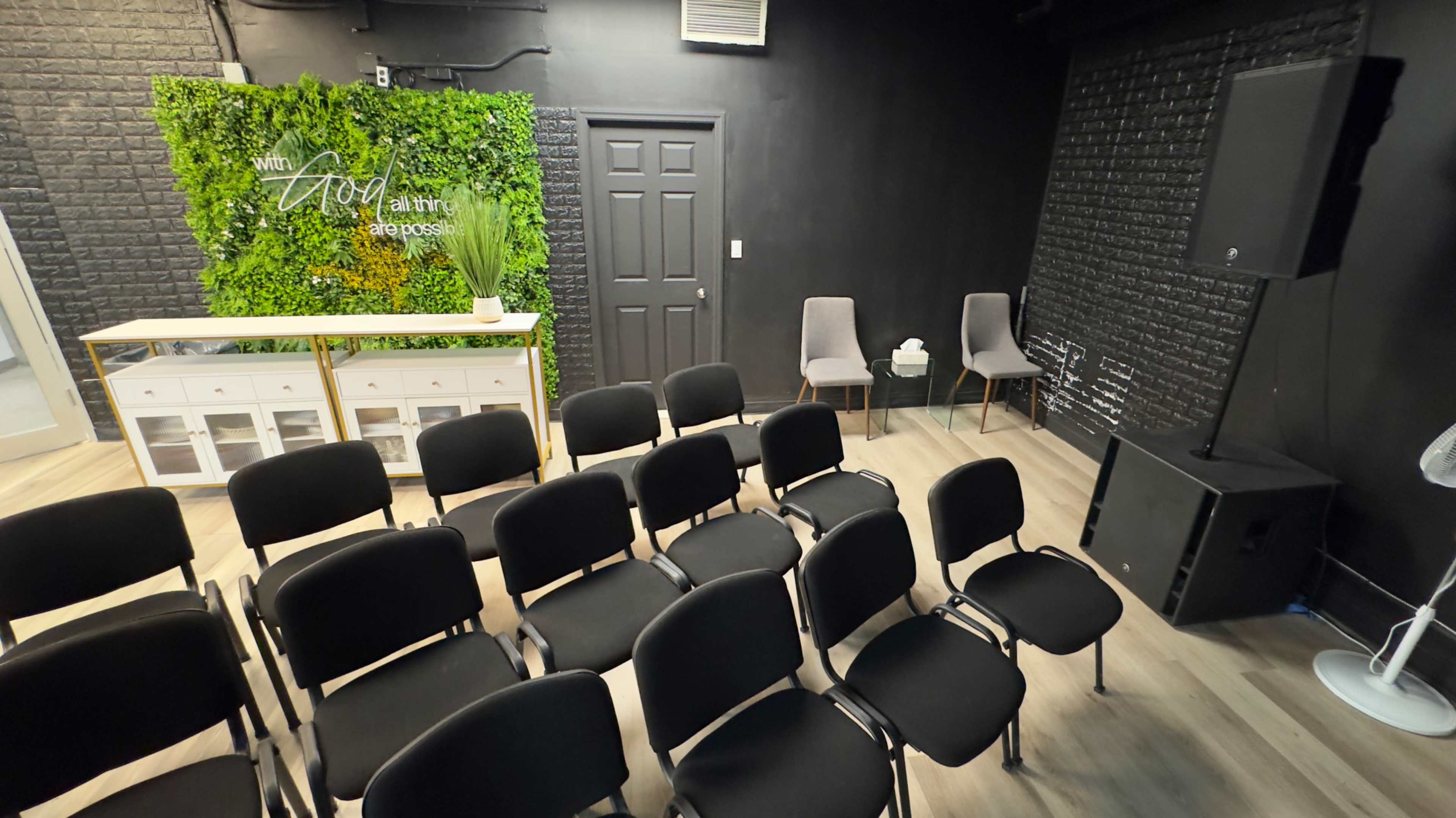 A seating arrangement of black chairs facing a small stage in a modern room with green wall decorations and a white reception area.