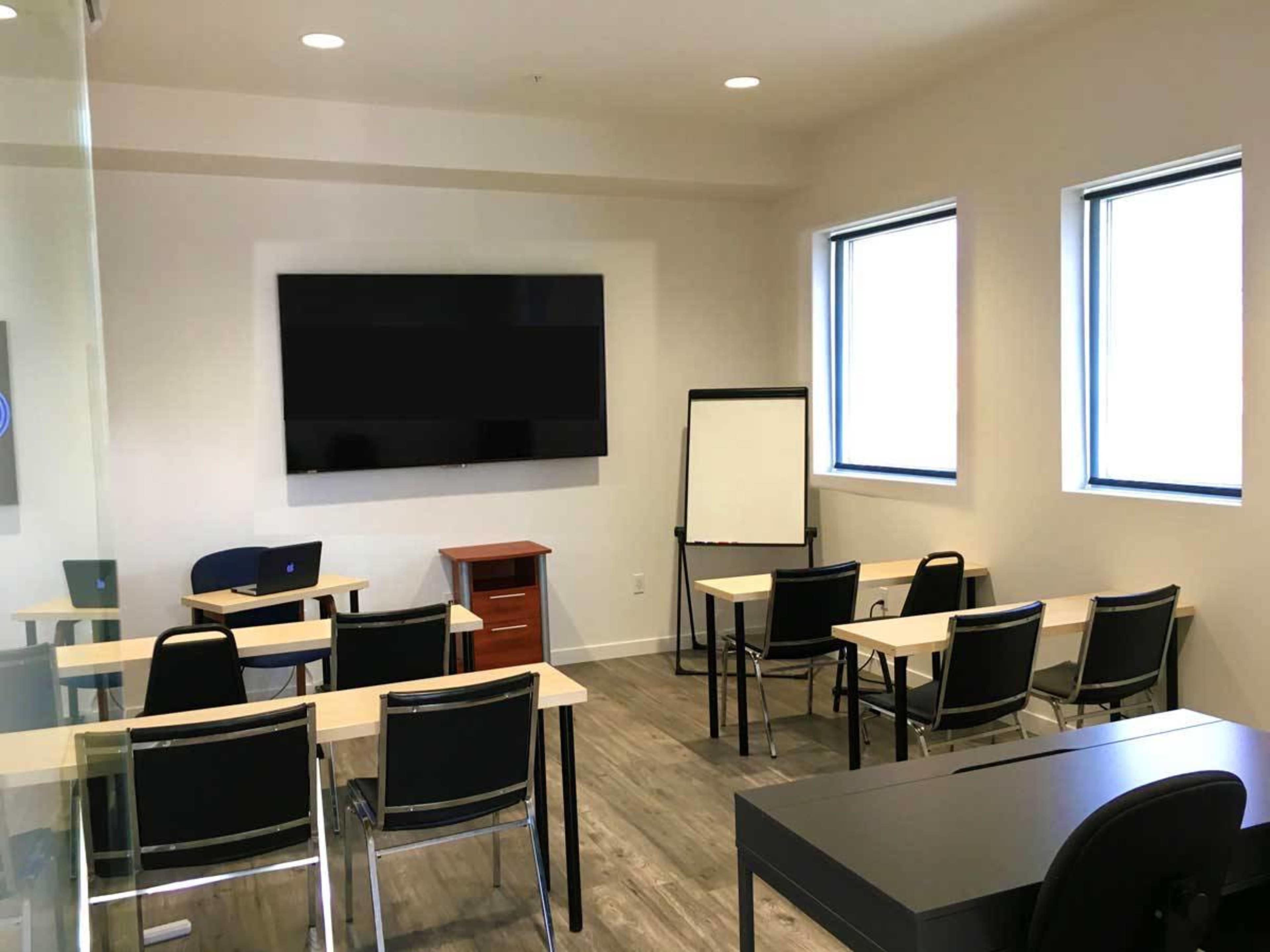 A modern classroom equipped with a large wall-mounted screen, several tables, chairs, and a writing board.