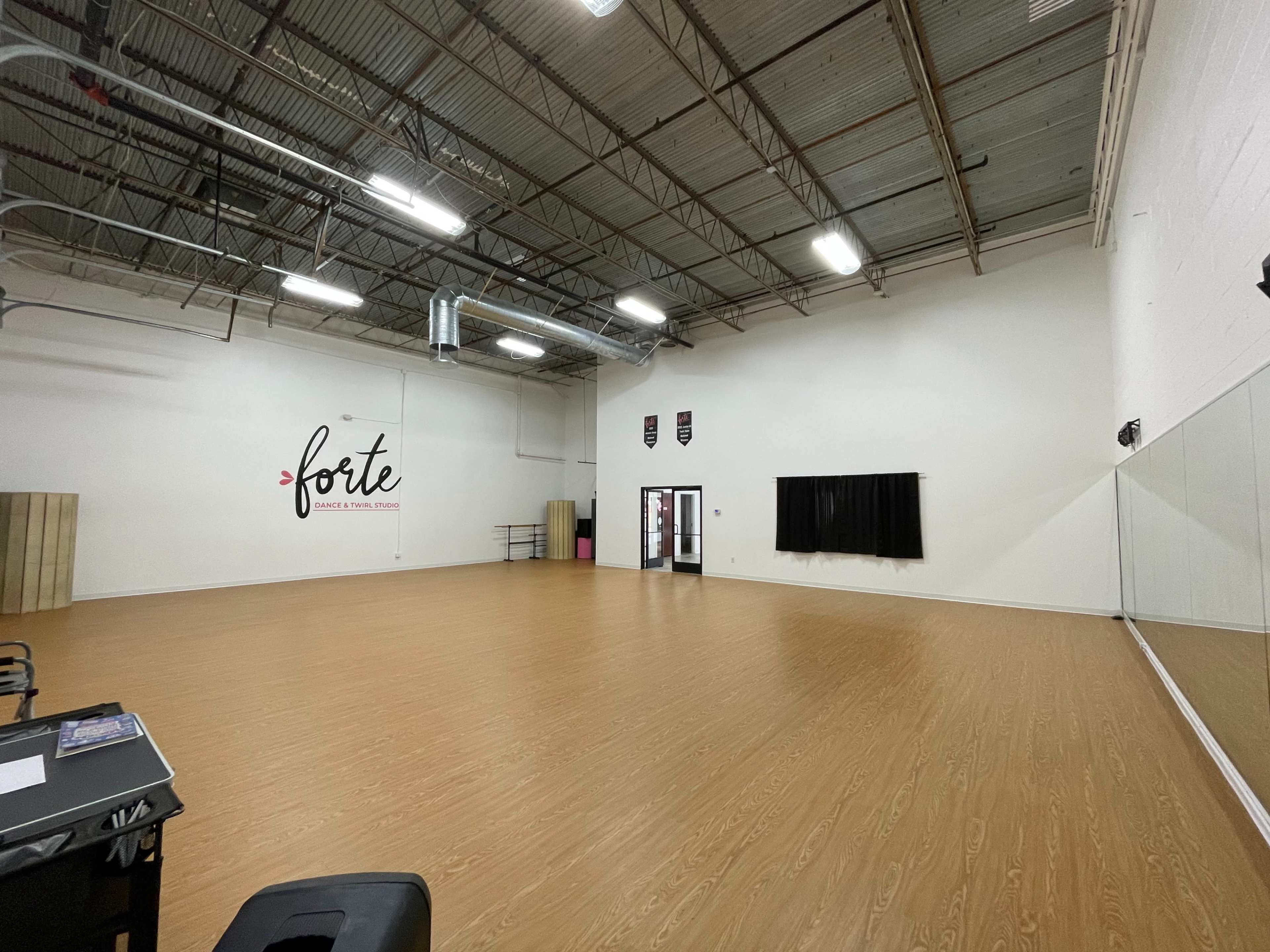 A spacious dance studio with wooden flooring, mirrors on one wall, and a large empty area.
