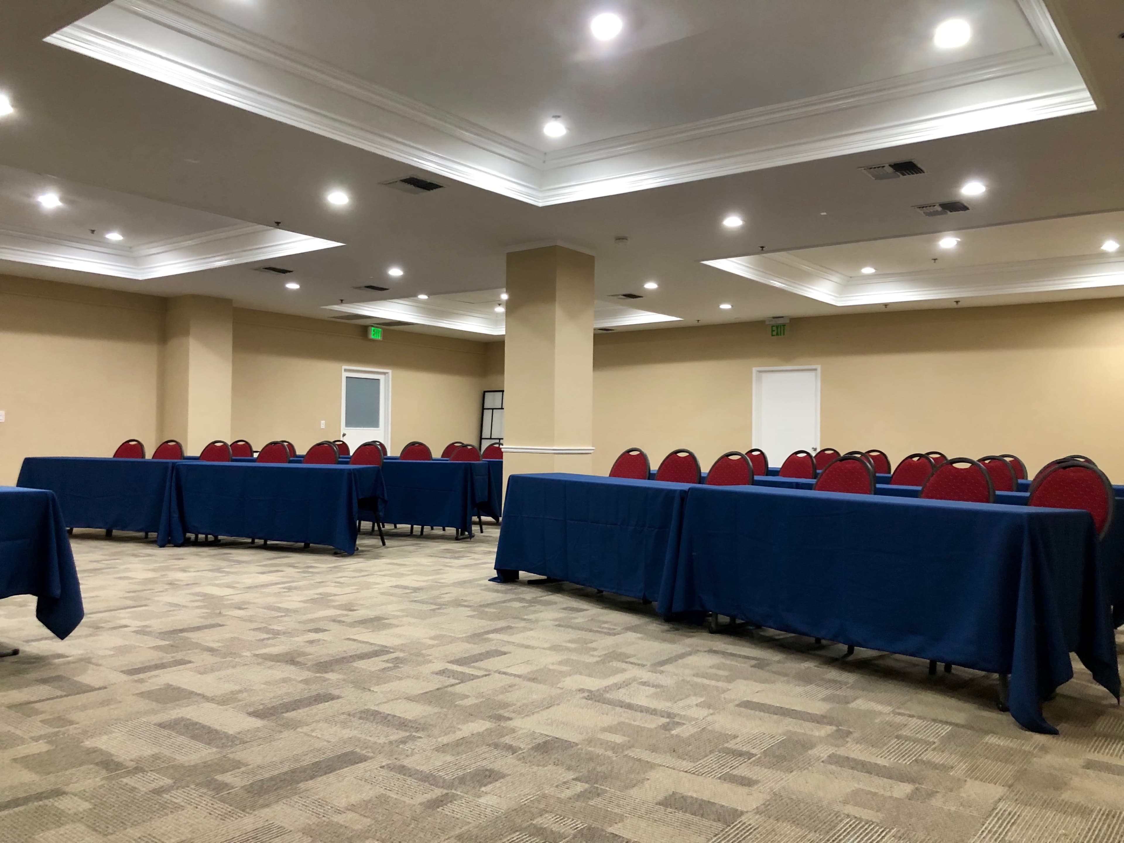 A spacious room with rows of tables covered in blue tablecloths and red chairs, arranged for a meeting or event.