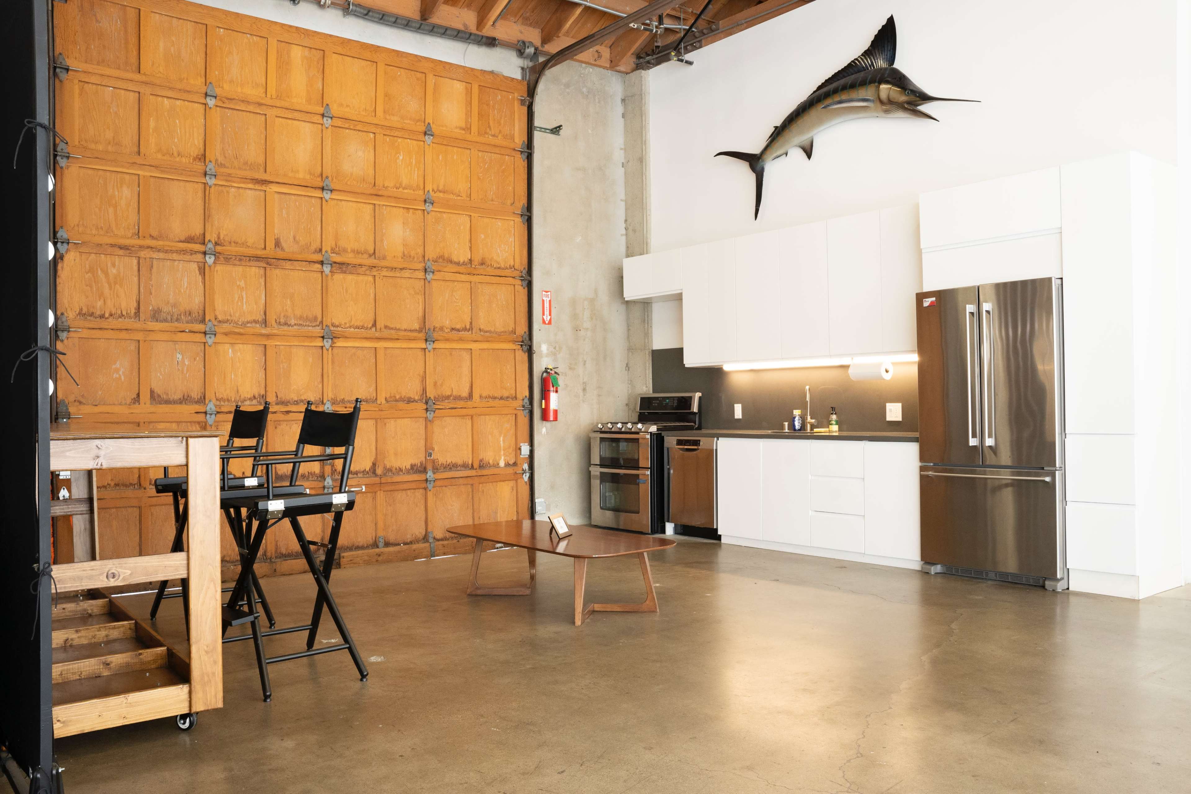 A modern kitchen and living area with a large wooden garage door, a mounted fish on the wall, and minimalistic furniture.