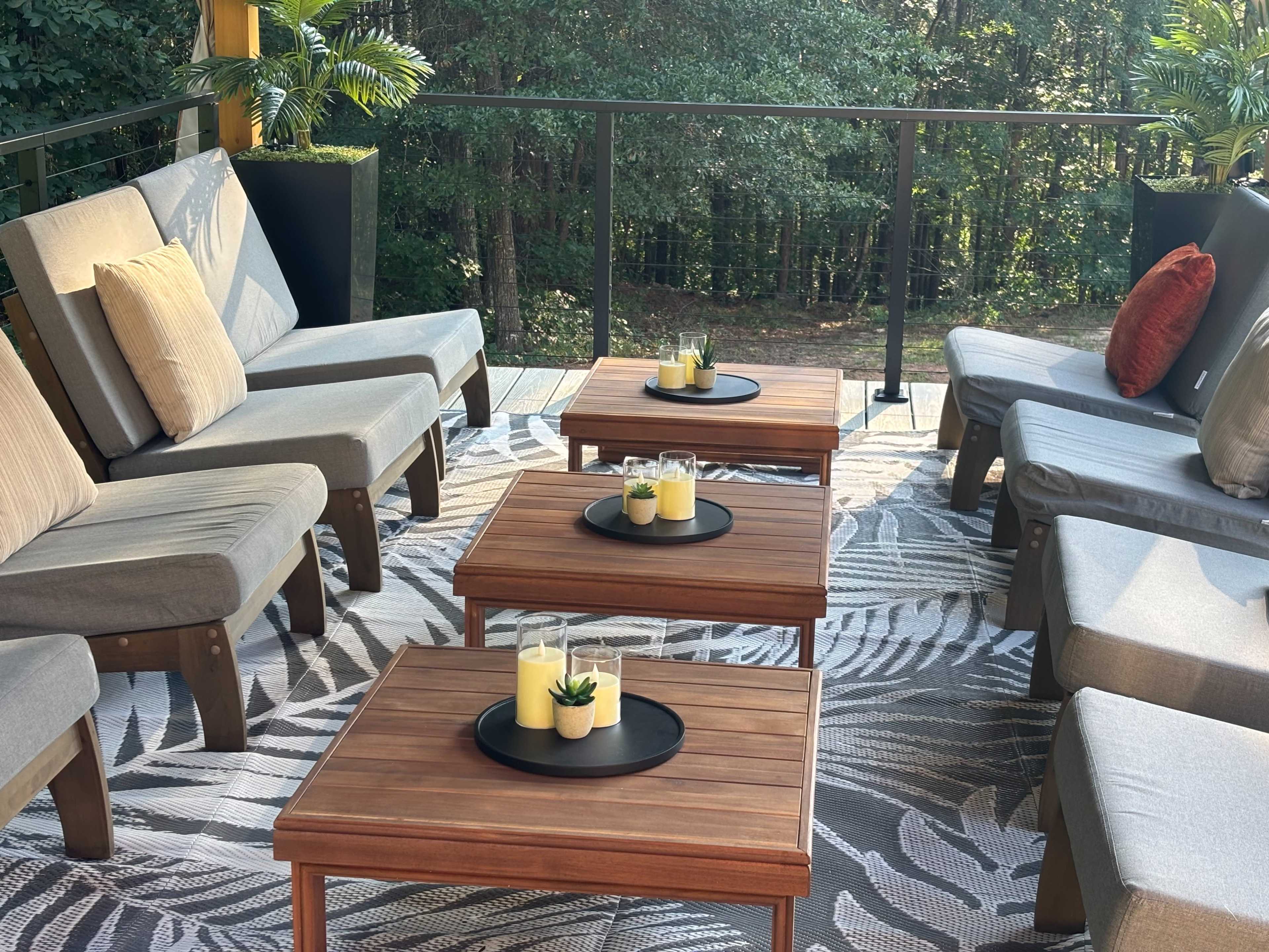 The image shows a cozy outdoor seating area with gray lounge chairs and wooden tables adorned with candles and small plants.