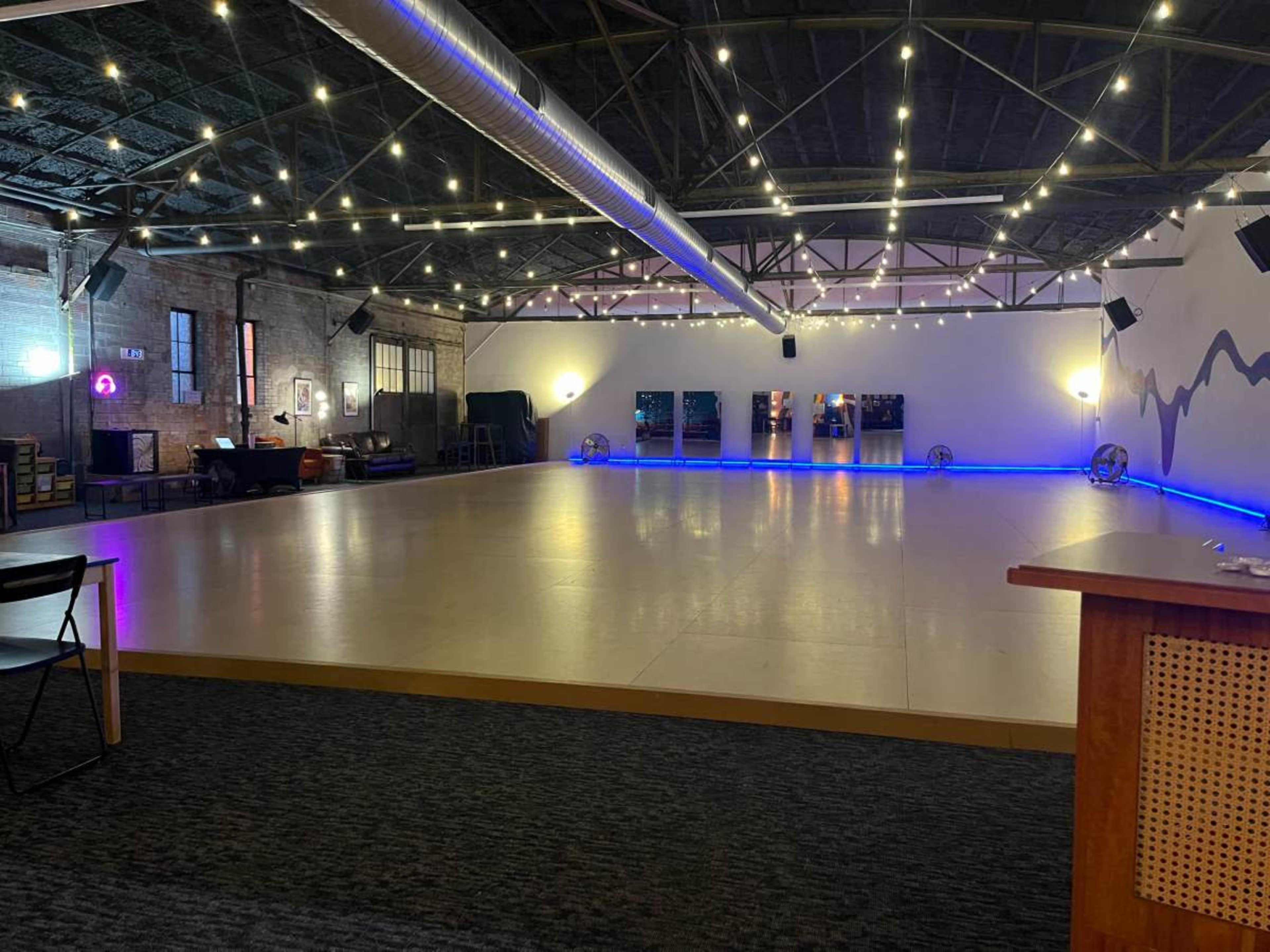 The image shows a spacious indoor venue with a polished floor, soft lighting, and decorative string lights hanging from the ceiling.