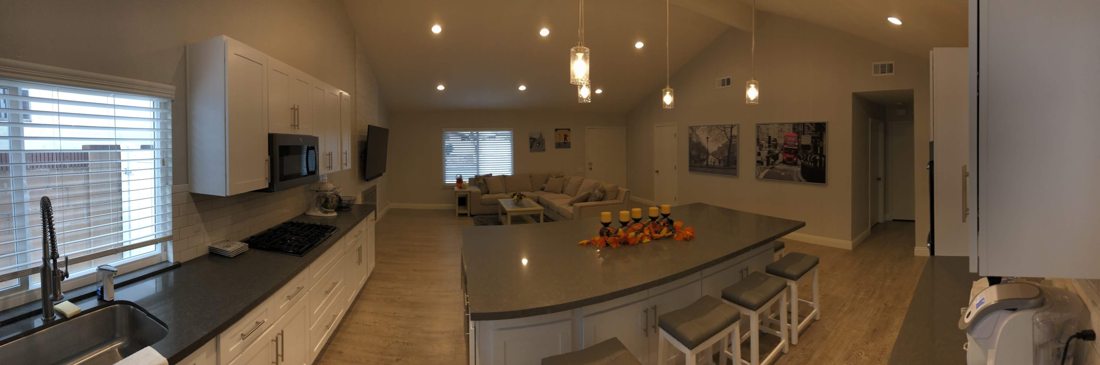A modern kitchen with a central island, white cabinetry, and a living area with a sofa, all featuring soft lighting and neutral colors.