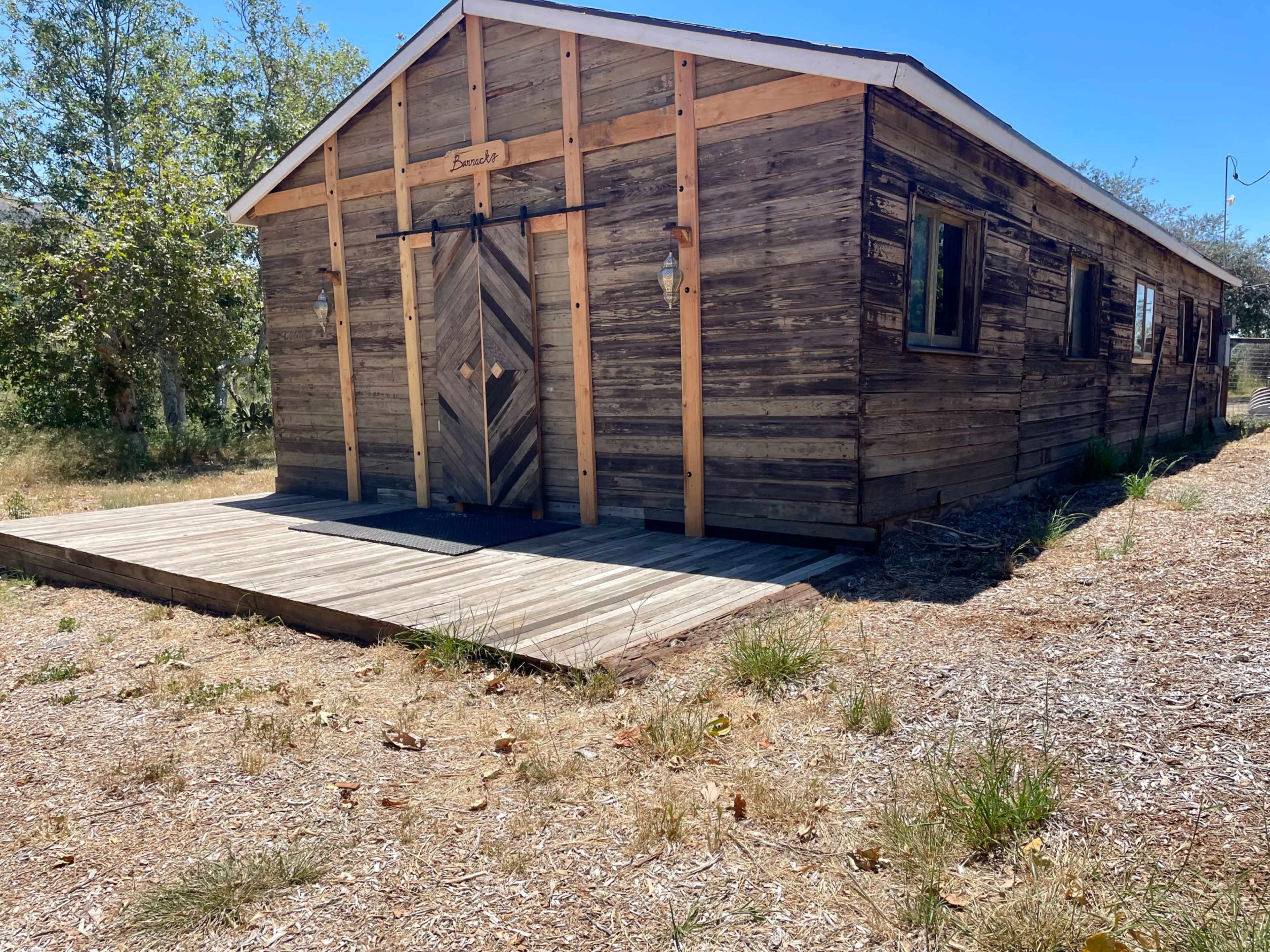A wooden building with a sloped roof features a front porch and decorative door on a grassy lot.