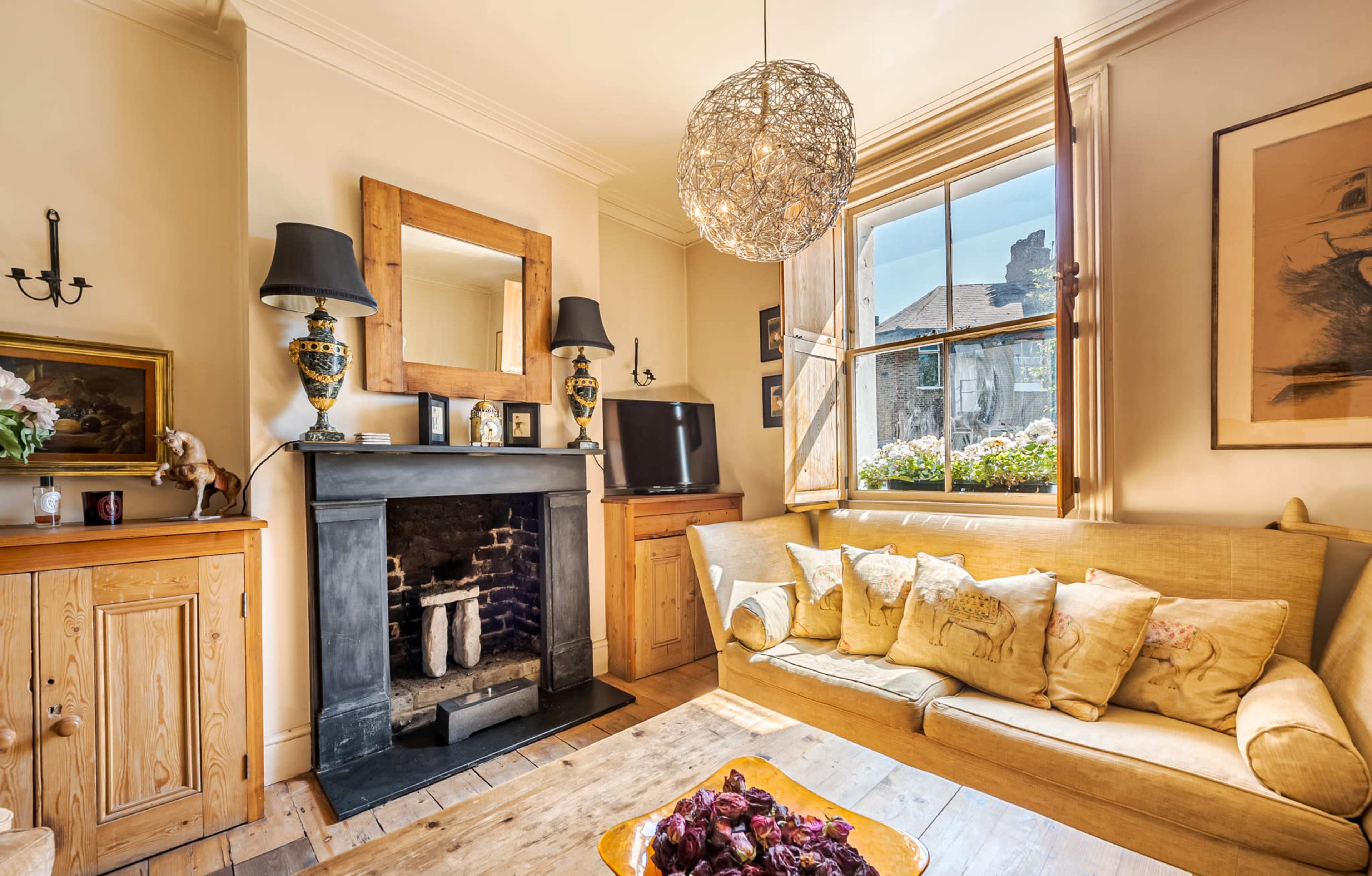 The image shows a cozy living room with a textured sofa, a fireplace, and large windows that open to a view outside.