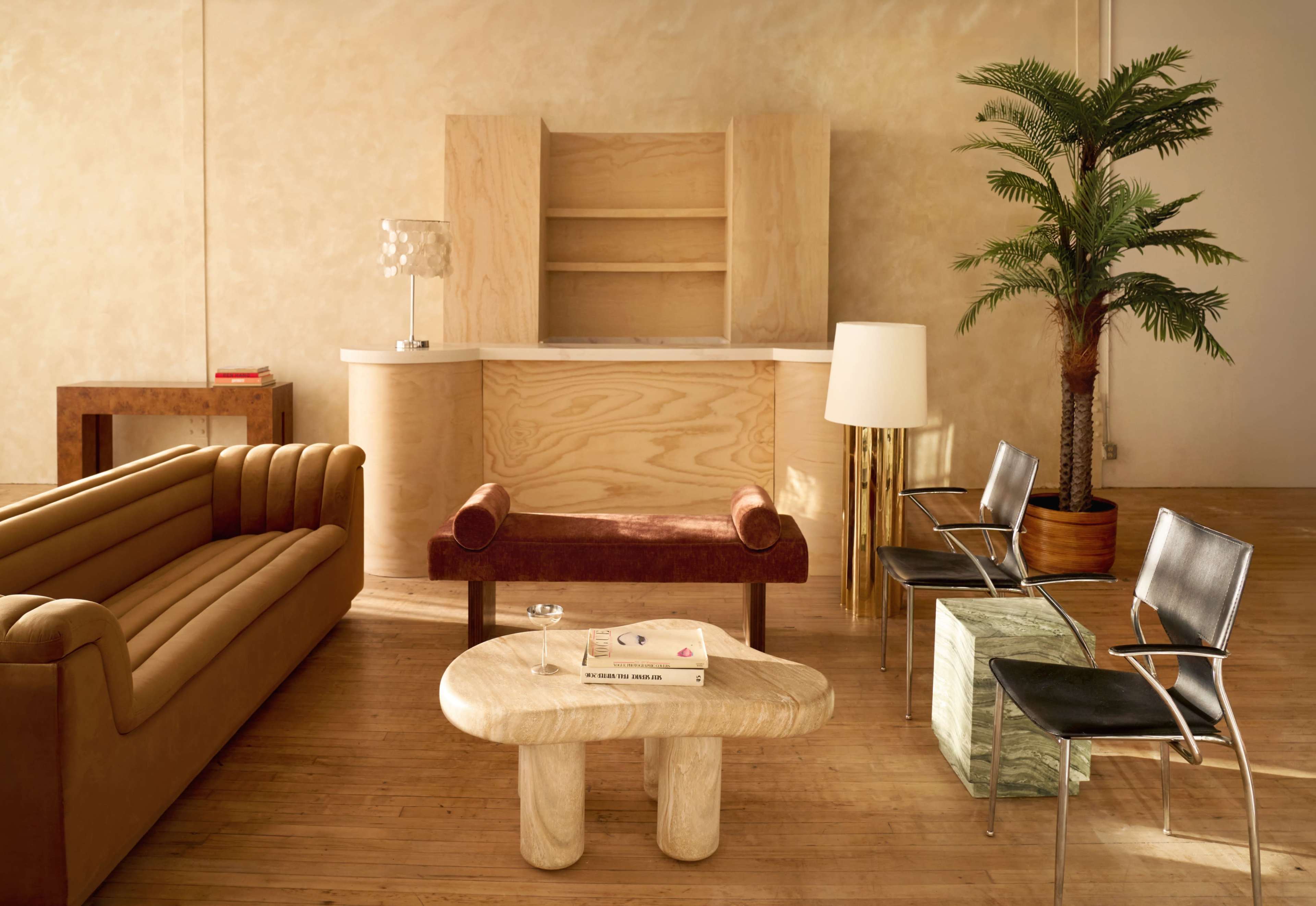 The image features a modern interior space with a wooden reception desk, a brown sofa, a burgundy chair, a wooden coffee table, and various decorative plants and light fixtures.