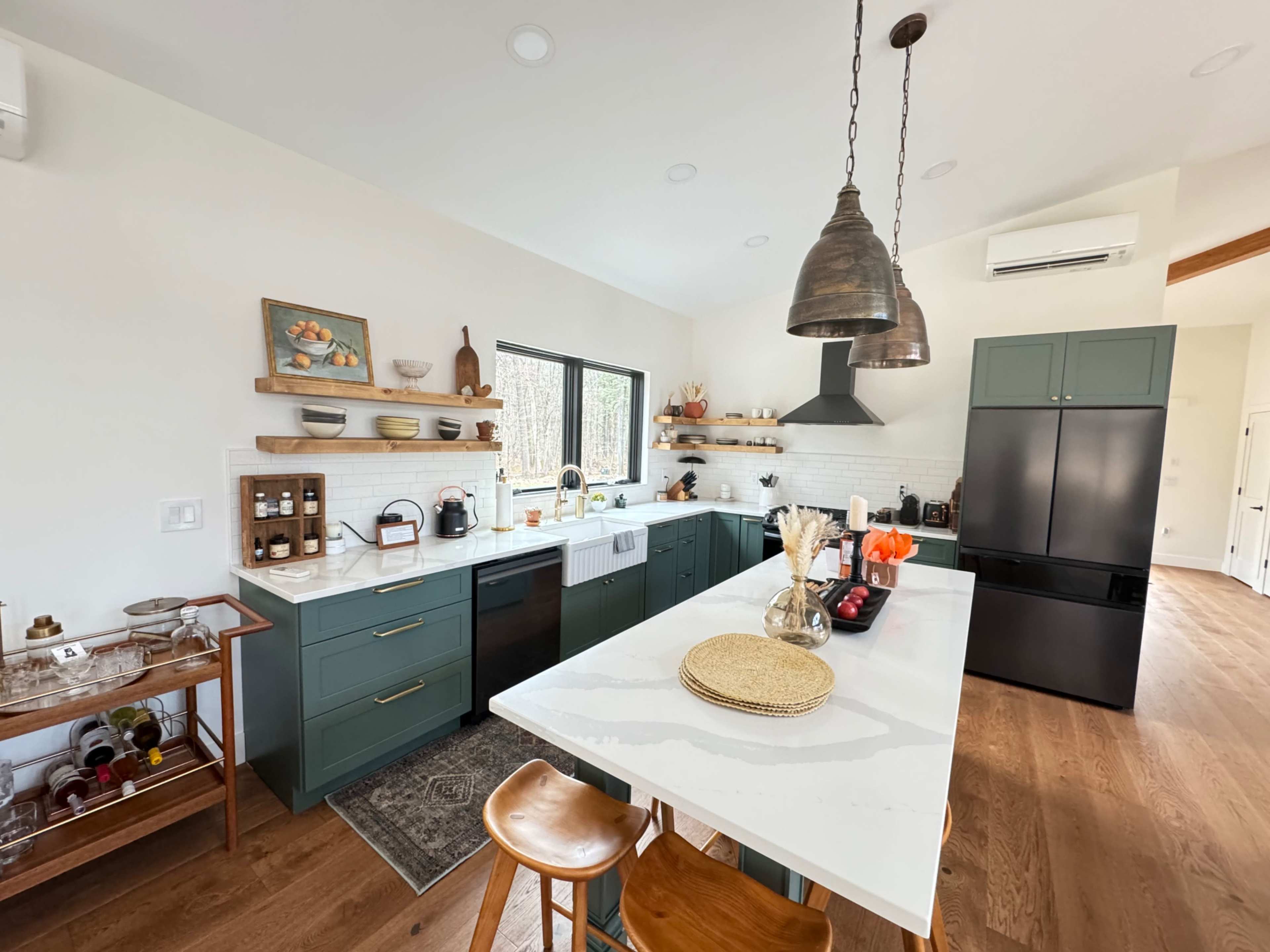 The image shows a modern kitchen featuring green cabinetry, a large white island with bar seating, and various kitchen appliances and accessories arranged neatly on open shelves.