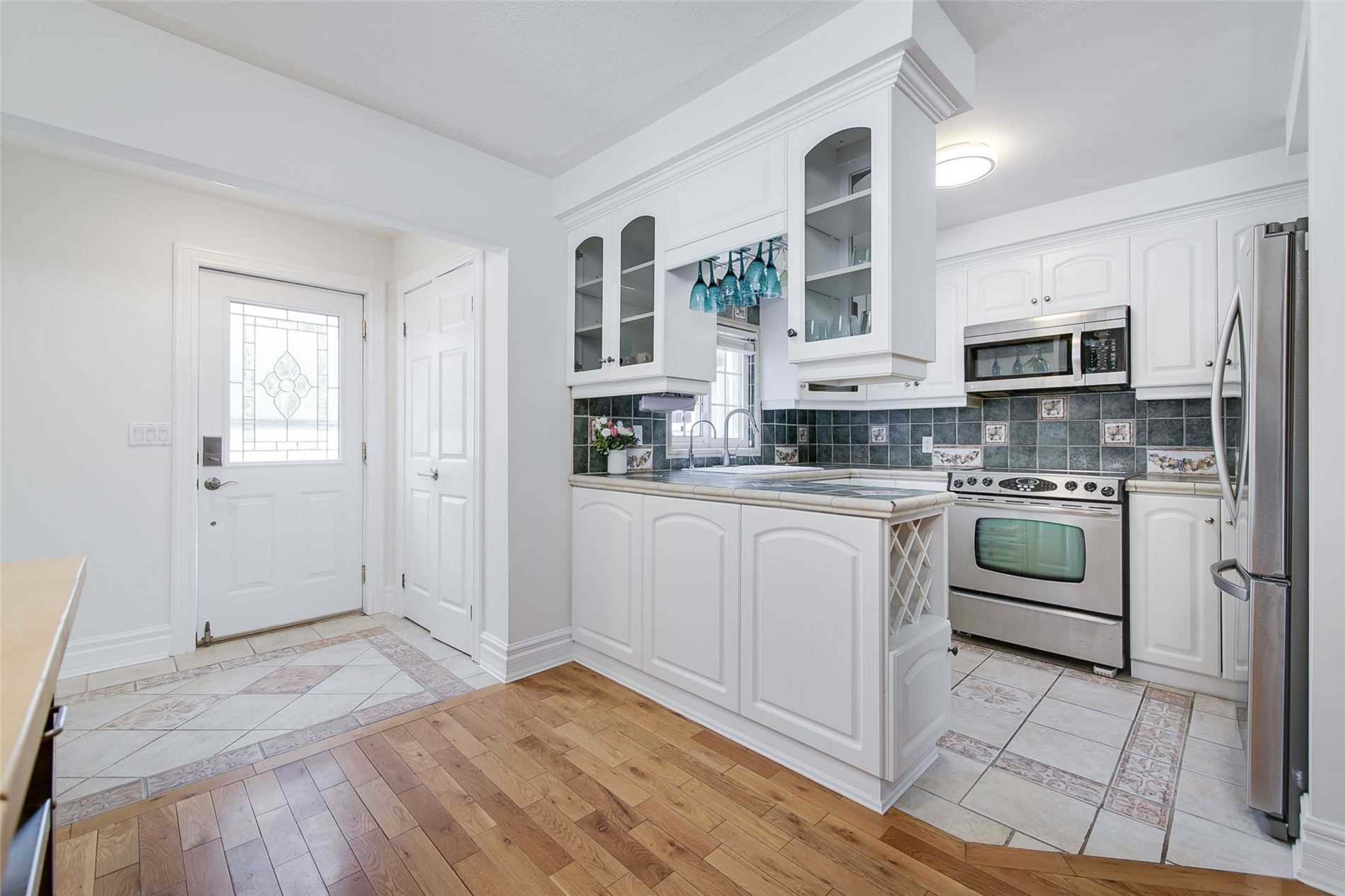 A well-lit kitchen featuring white cabinetry, stainless steel appliances, and tiled flooring, with a door leading outside.