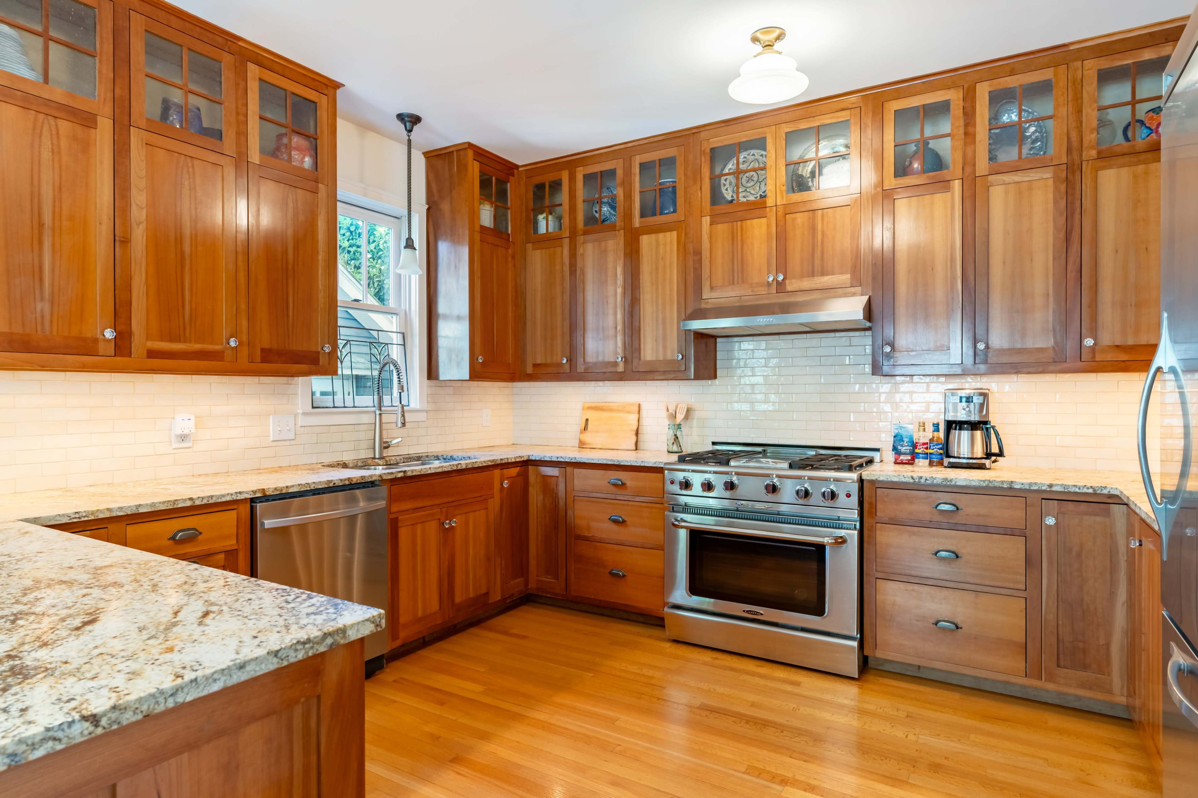 The image shows a modern kitchen featuring wooden cabinetry, granite countertops, and stainless steel appliances.