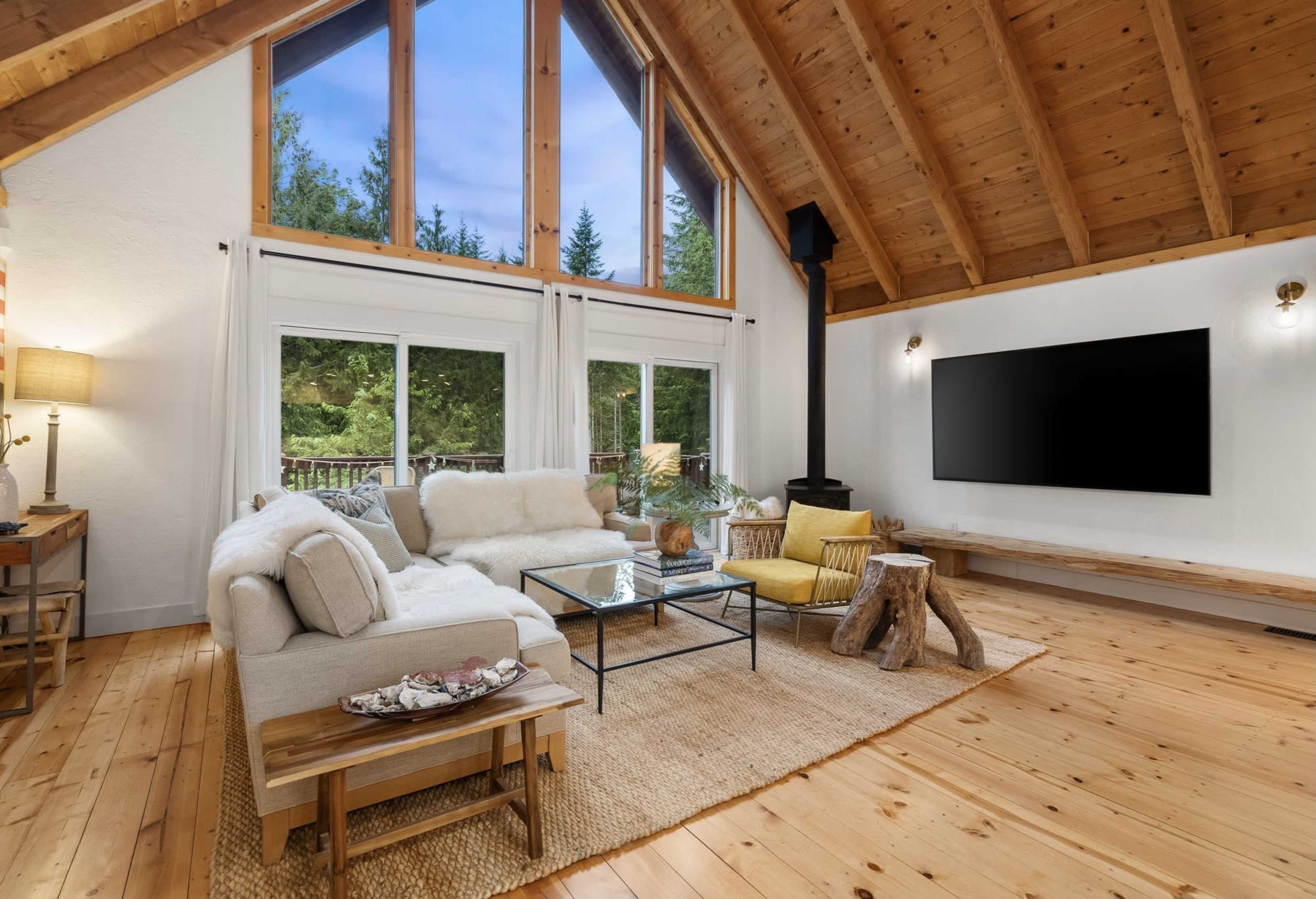 A spacious living room features a large sectional sofa, a glass coffee table, and a flat-screen TV mounted on a wooden wall.