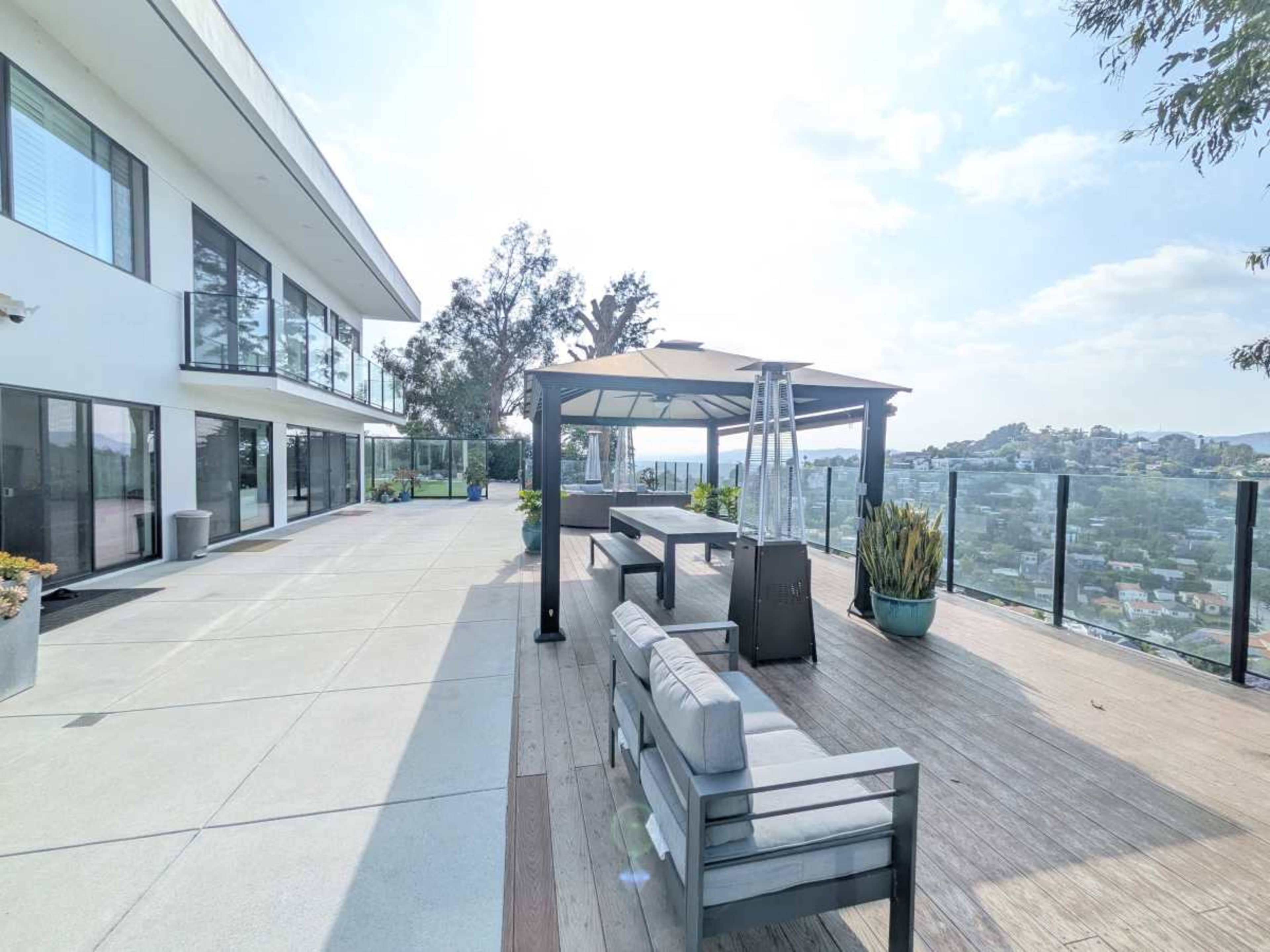 The image shows a modern outdoor patio area with seating, a canopy, and a view of the surrounding landscape.