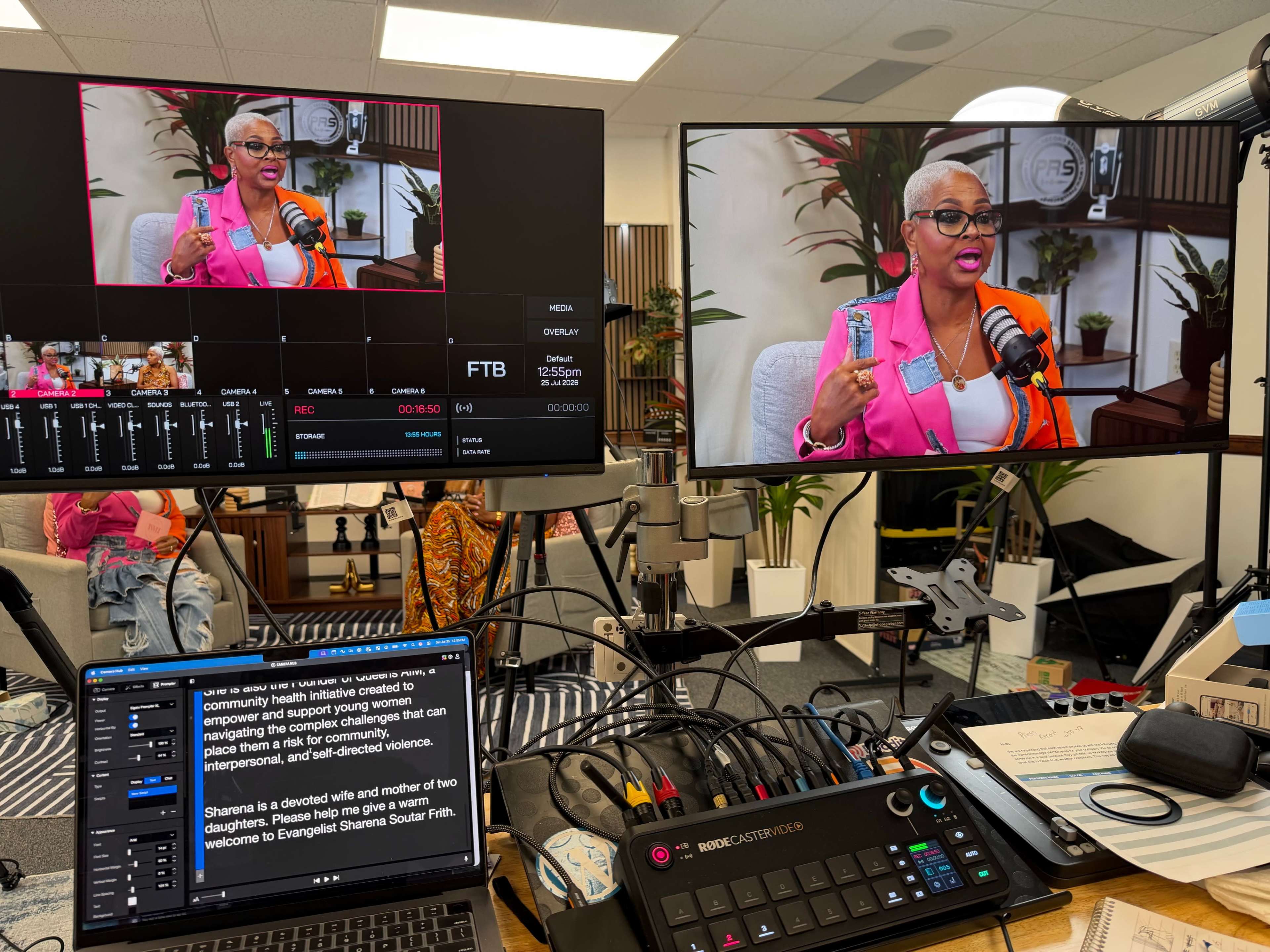 The image shows a video production setup featuring two large screens displaying a woman with glasses speaking, along with a laptop and various equipment on a desk.