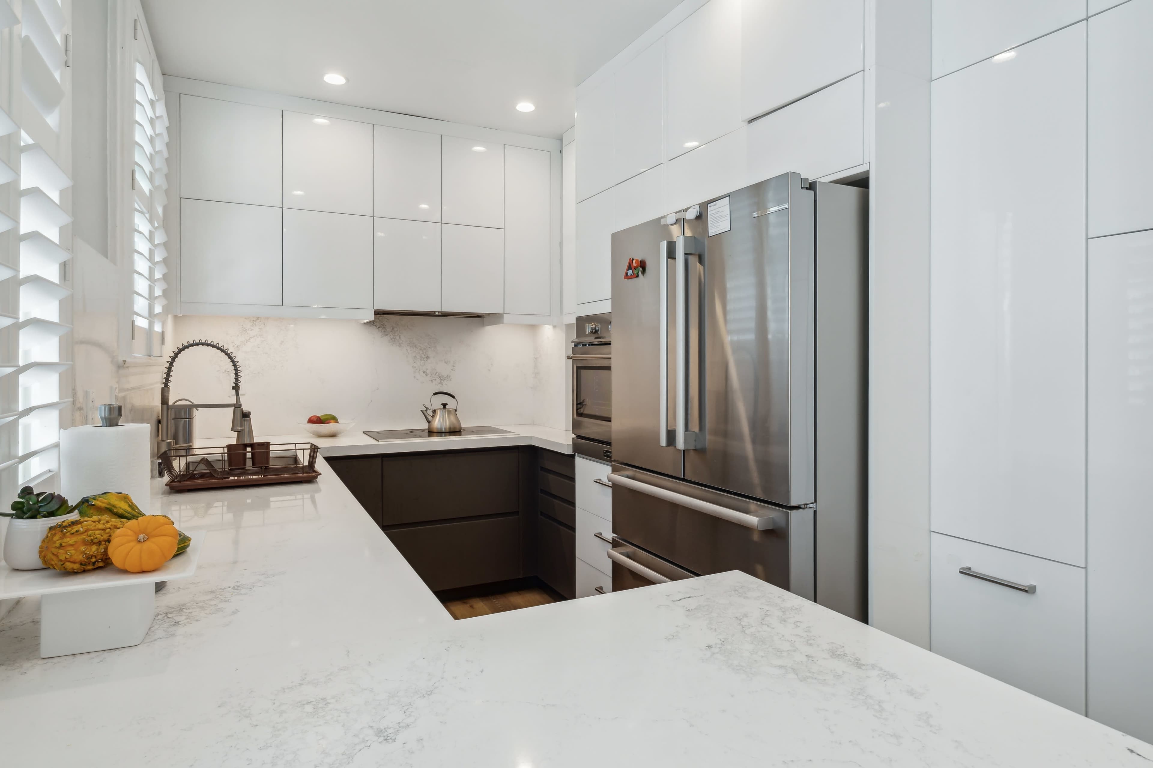 A modern kitchen featuring sleek white cabinetry, stainless steel appliances, and a marble countertop.