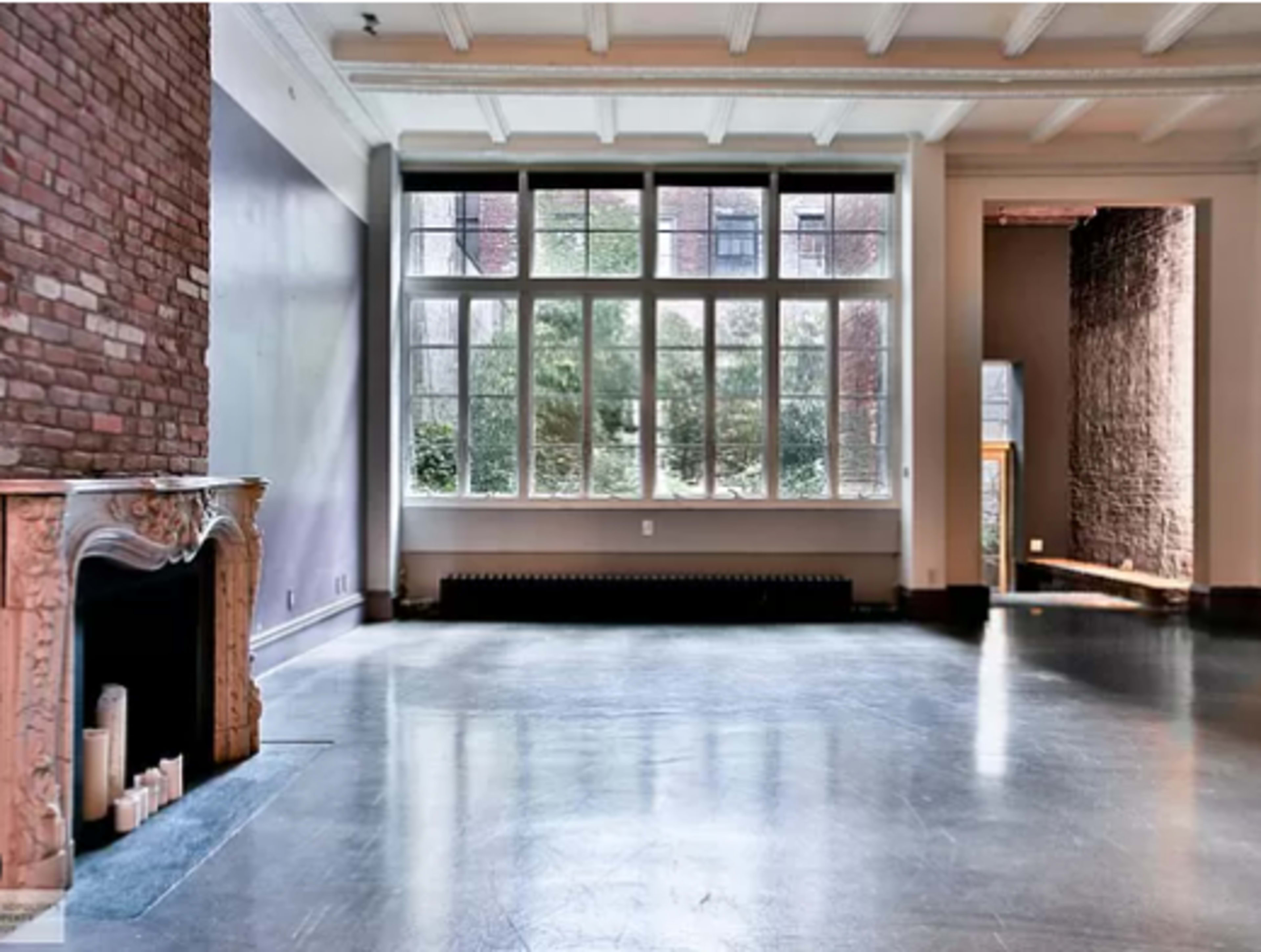 The image shows a spacious, empty room with large windows, hardwood flooring, and a decorative fireplace.