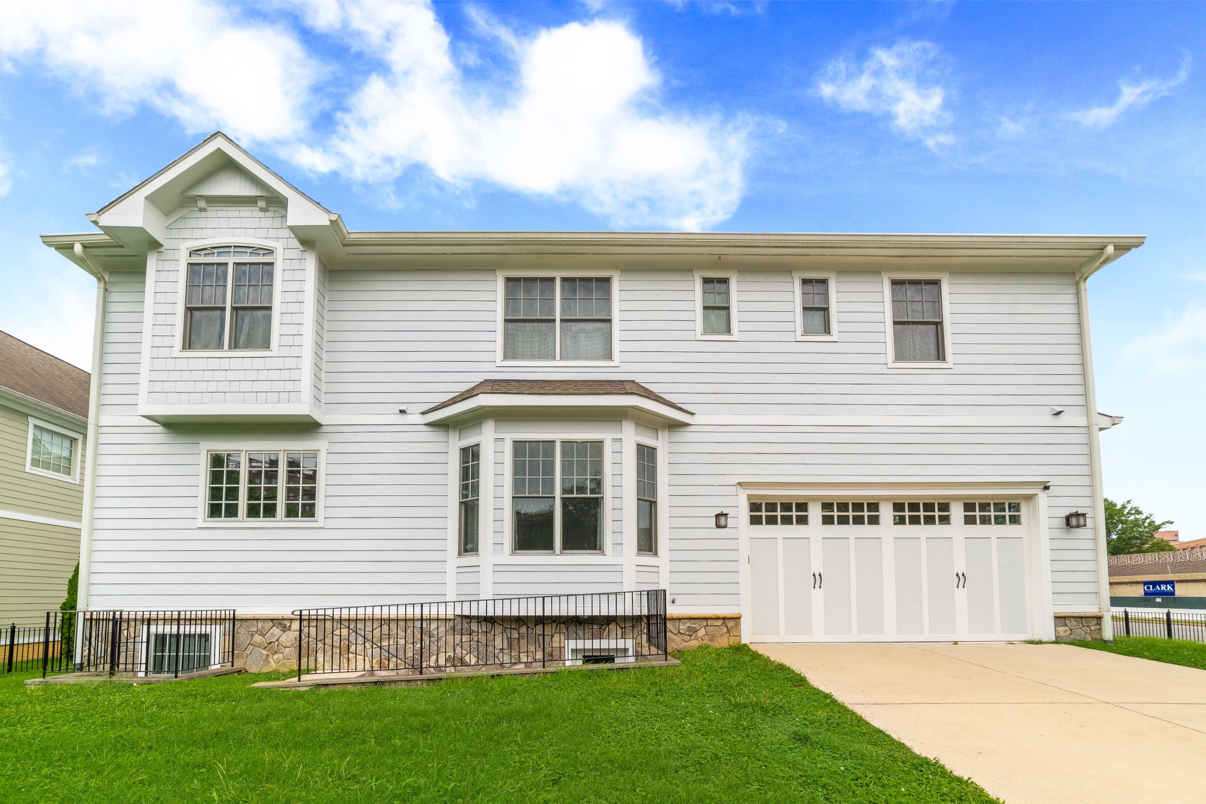 A white two-story house features a front bay window, four garage doors, and a manicured lawn.