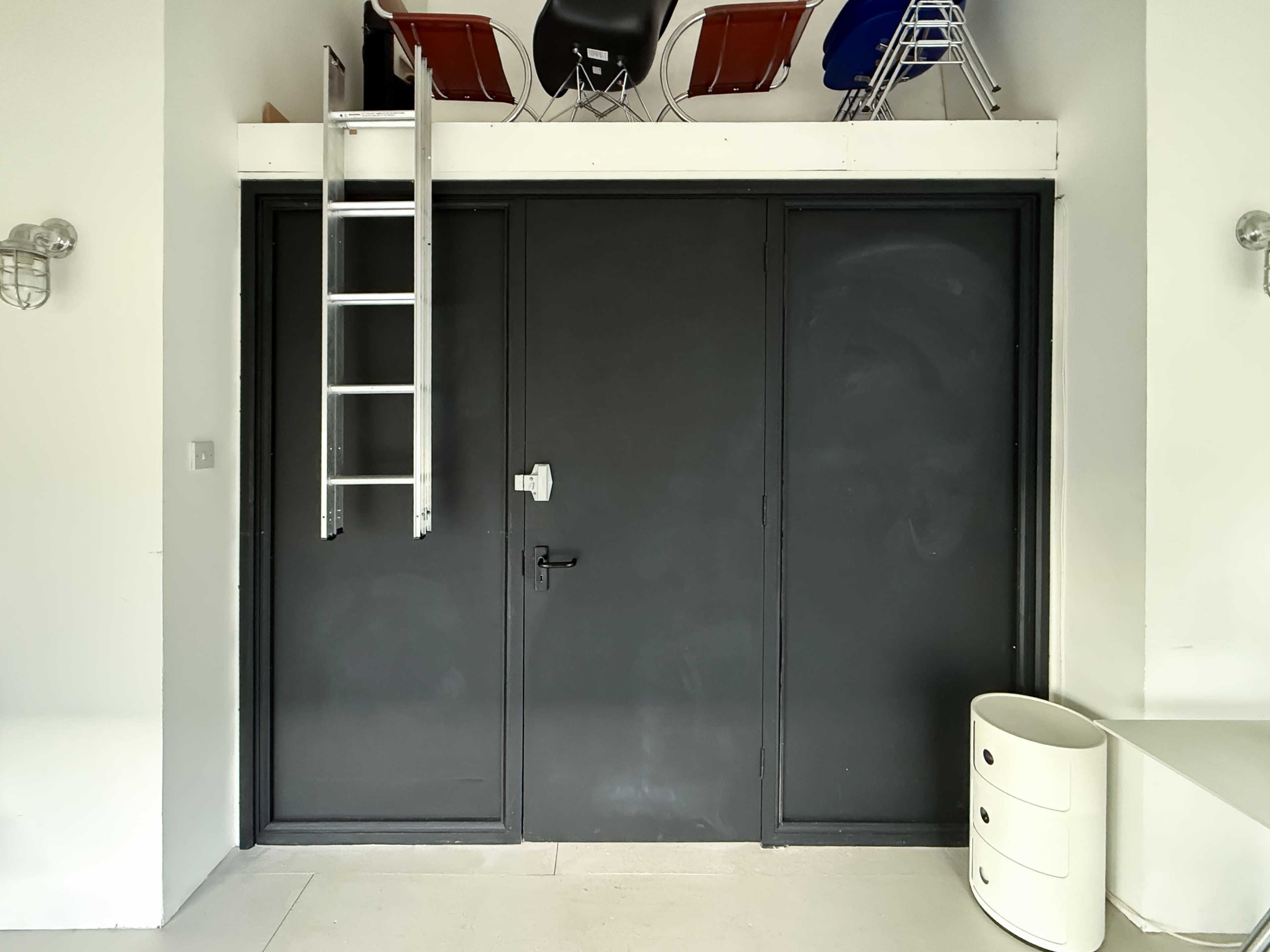 A black door with a ladder leaning against it is located in a minimalist room.