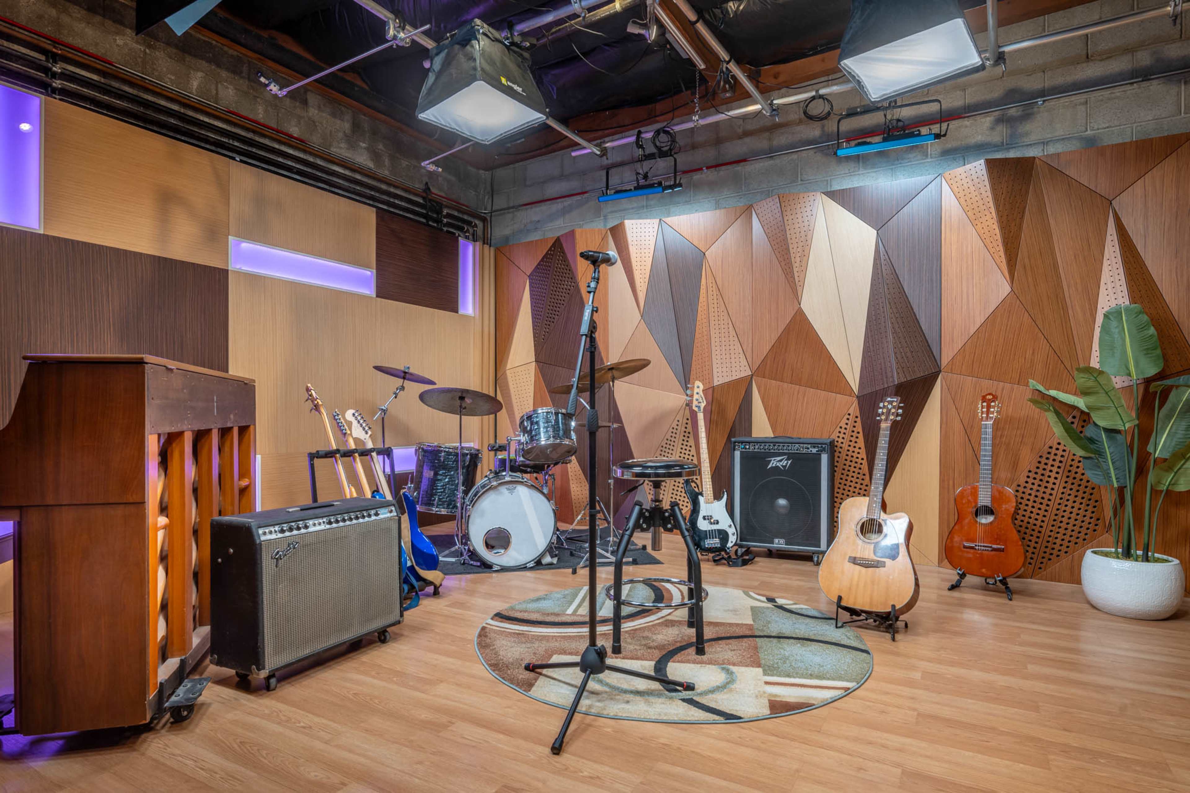 A music studio features a microphone on a stand, various musical instruments, and a patterned wooden accent wall.