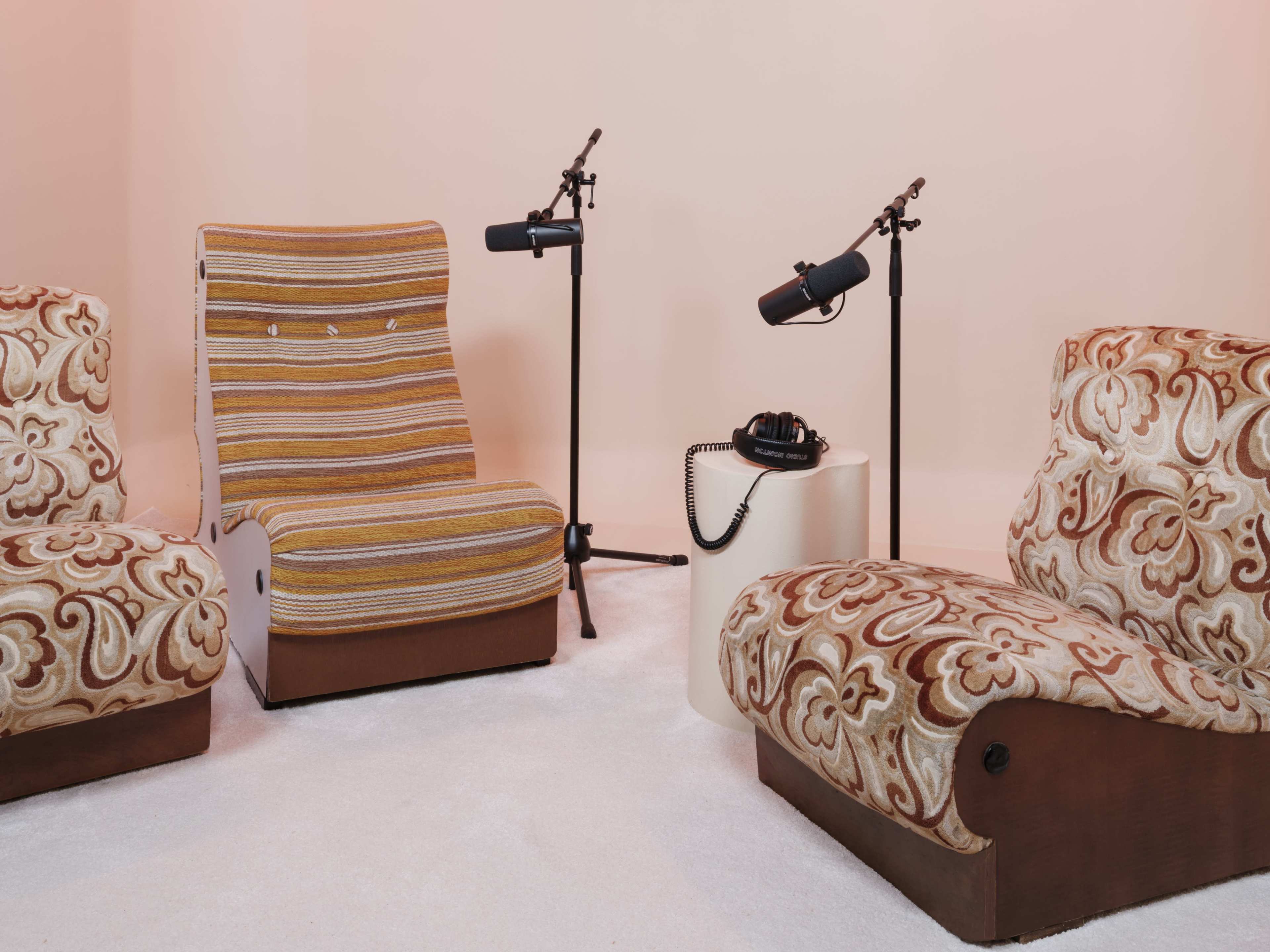 The scene features two vintage armchairs and a striped reclining chair, with microphones on stands and a telephone placed on a small round table.