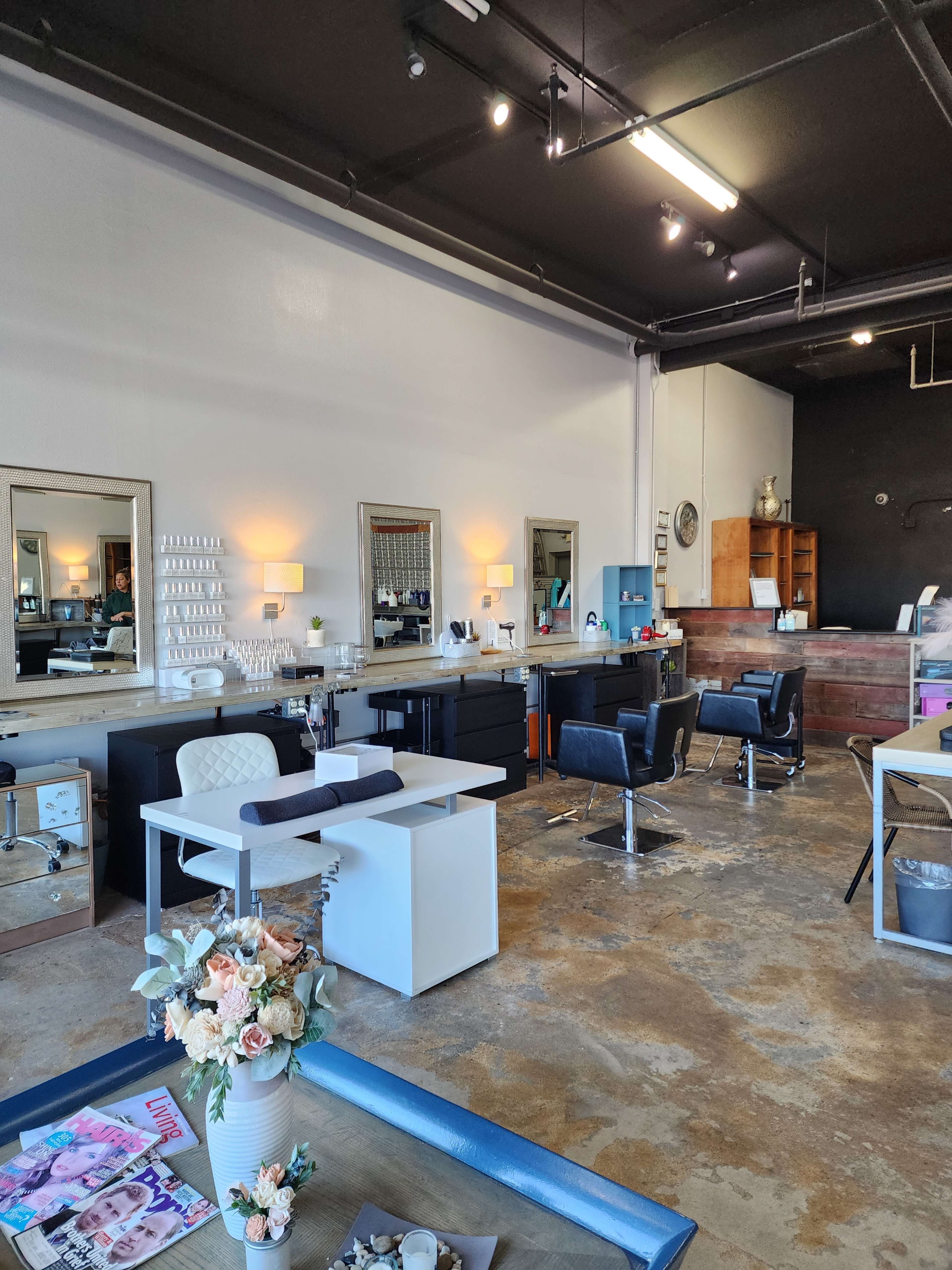 A brightly lit beauty salon with several styling stations, a waiting area, and polished concrete floors.