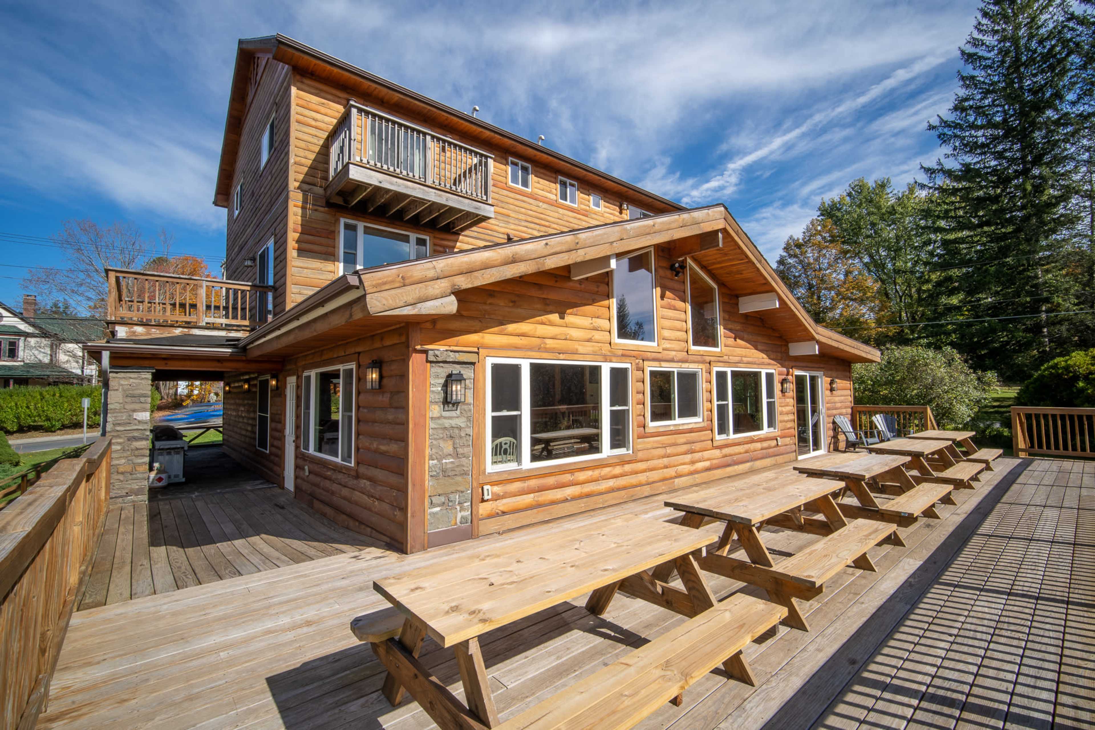 A three-story log cabin with multiple large windows and an outdoor deck featuring several picnic tables.