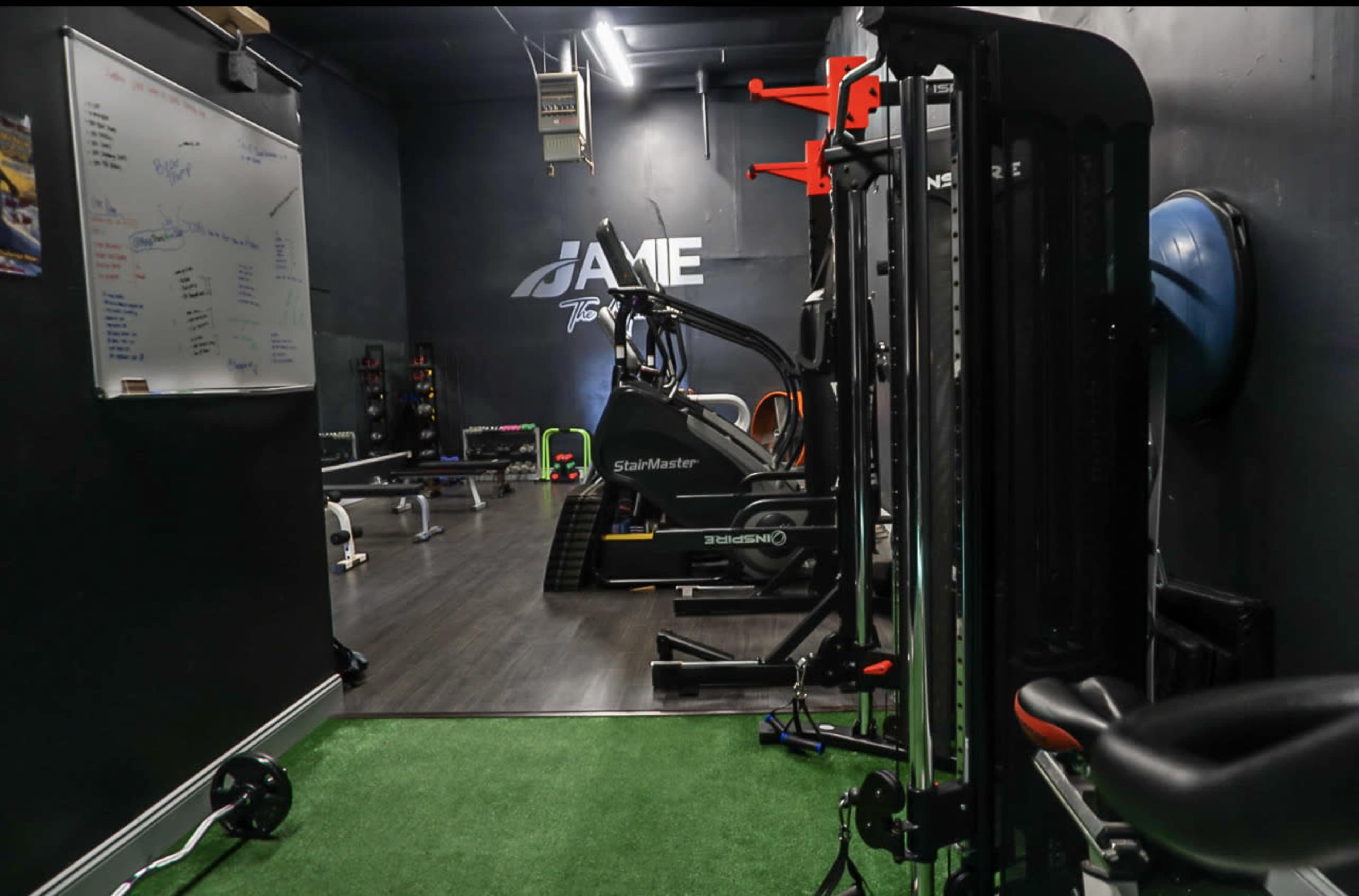 A fitness training area with various exercise equipment, including a stair climber and weight machines, on a wood and artificial turf floor.