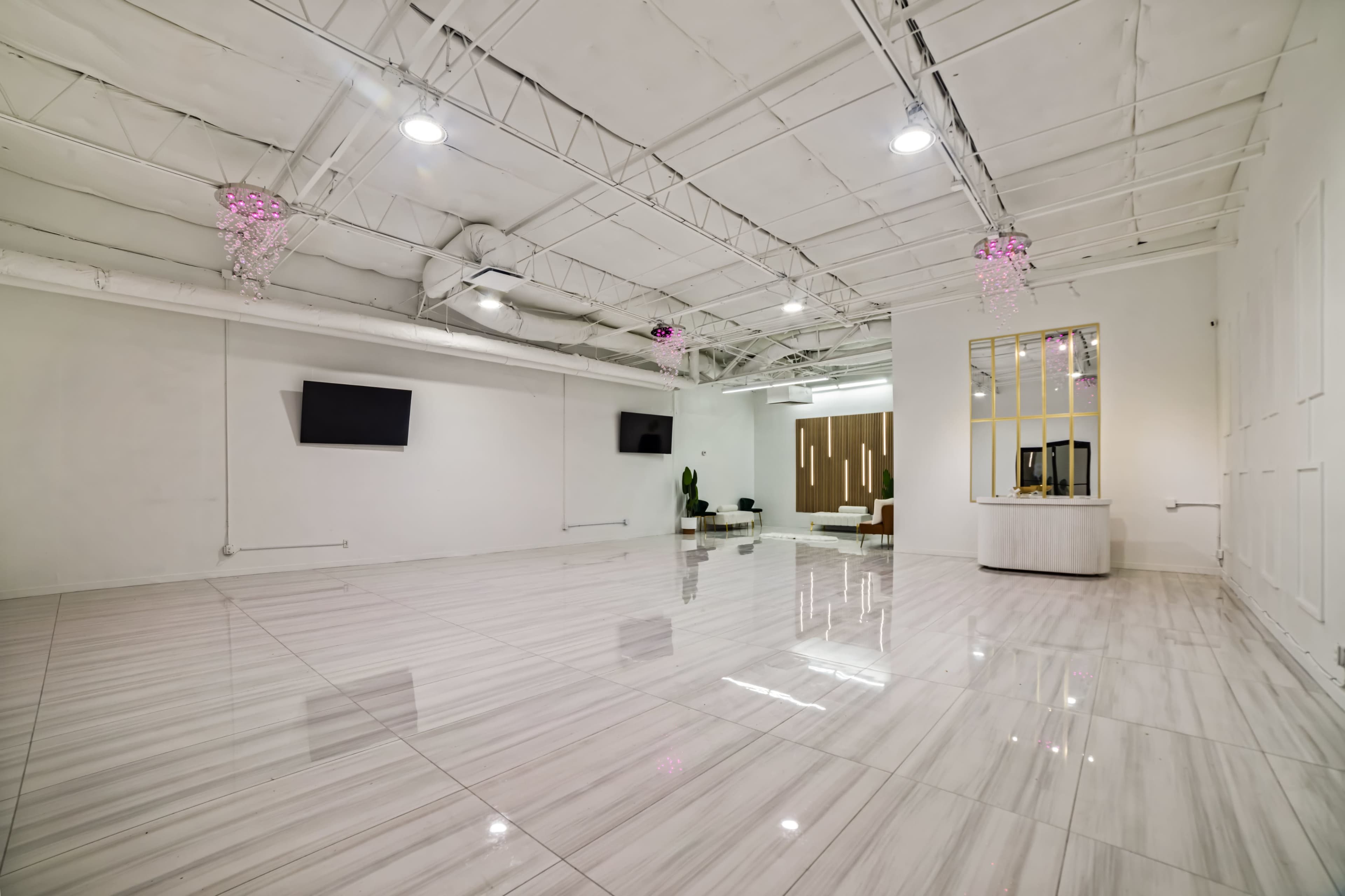 A large, empty studio space features white walls, shiny marble flooring, and modern lighting fixtures.