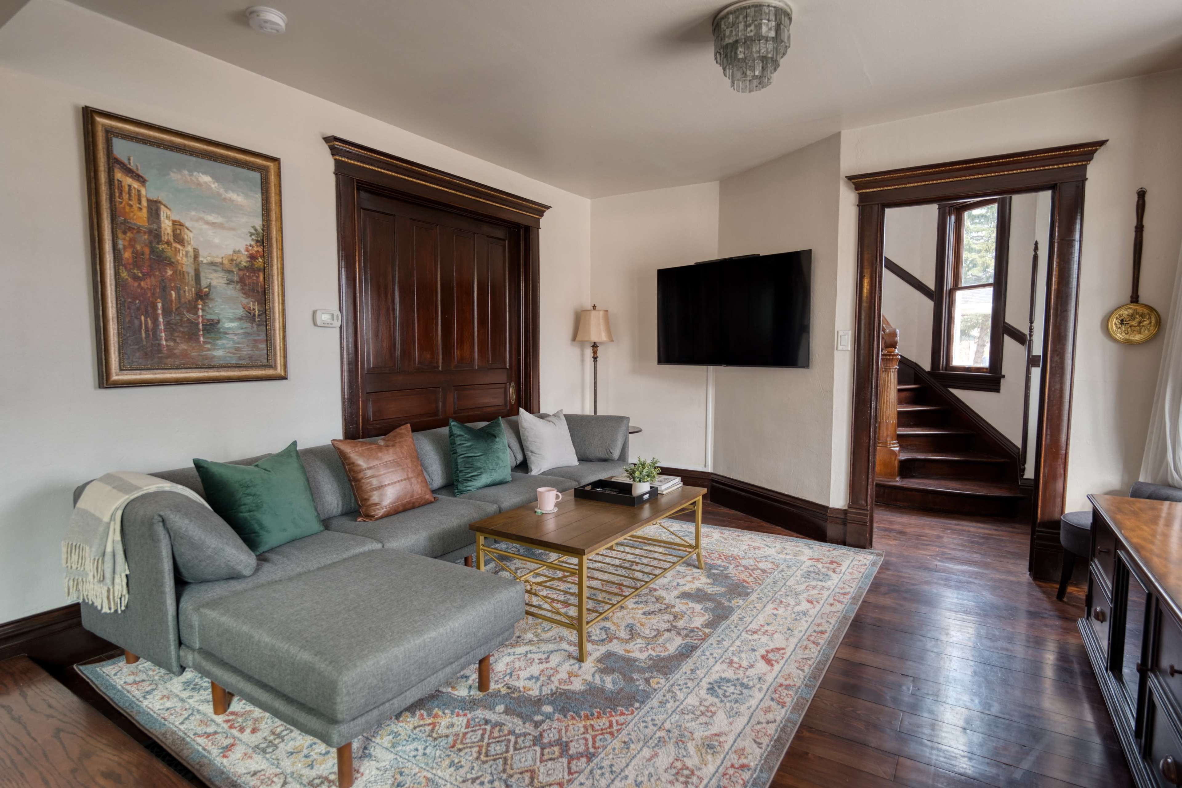 A cozy living room with a sectional sofa, a coffee table, a wall-mounted television, and a staircase leading to an upper level.