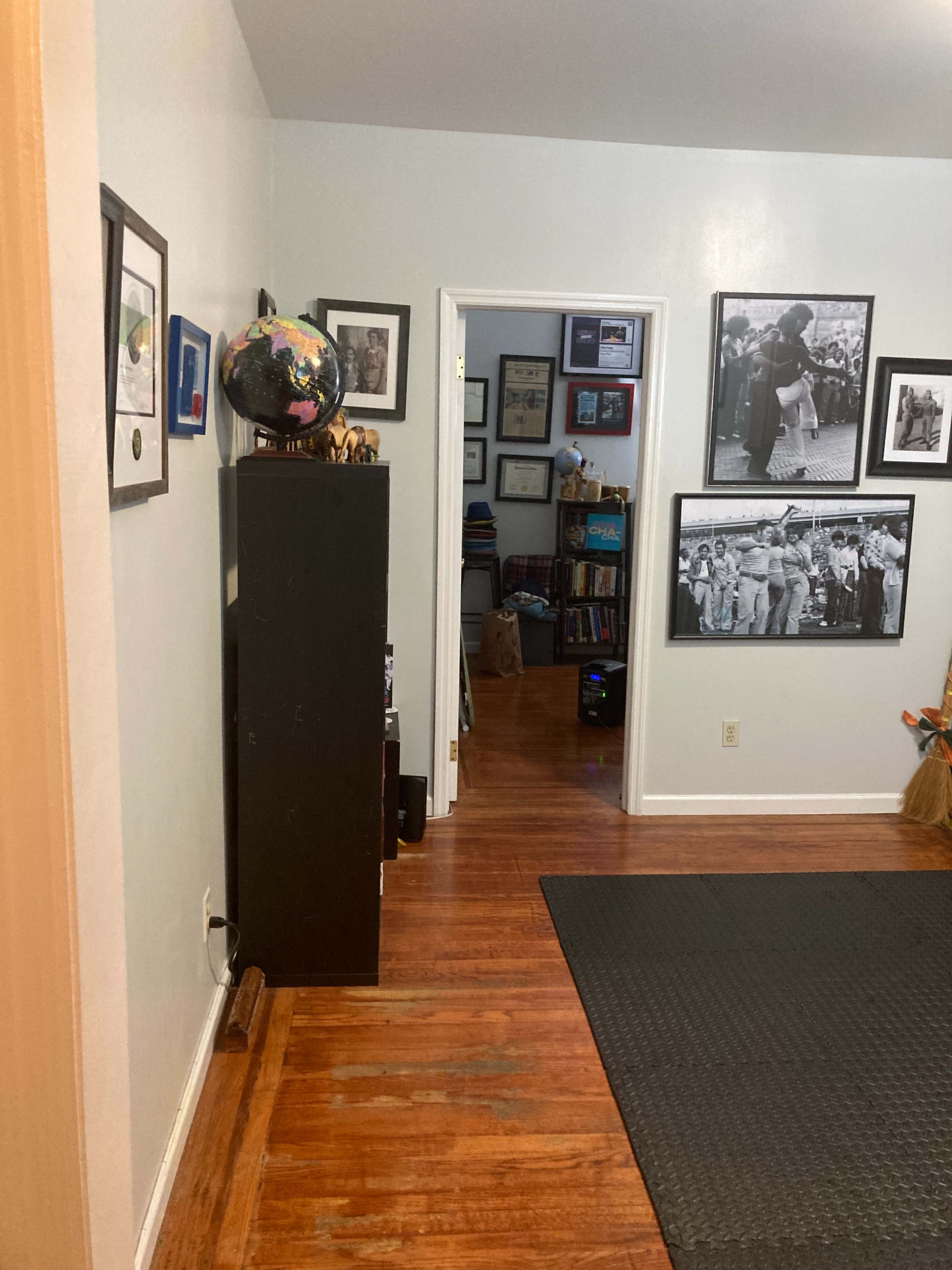 The image shows a hallway leading to a room with framed photographs on the walls and a globe atop a black cabinet.