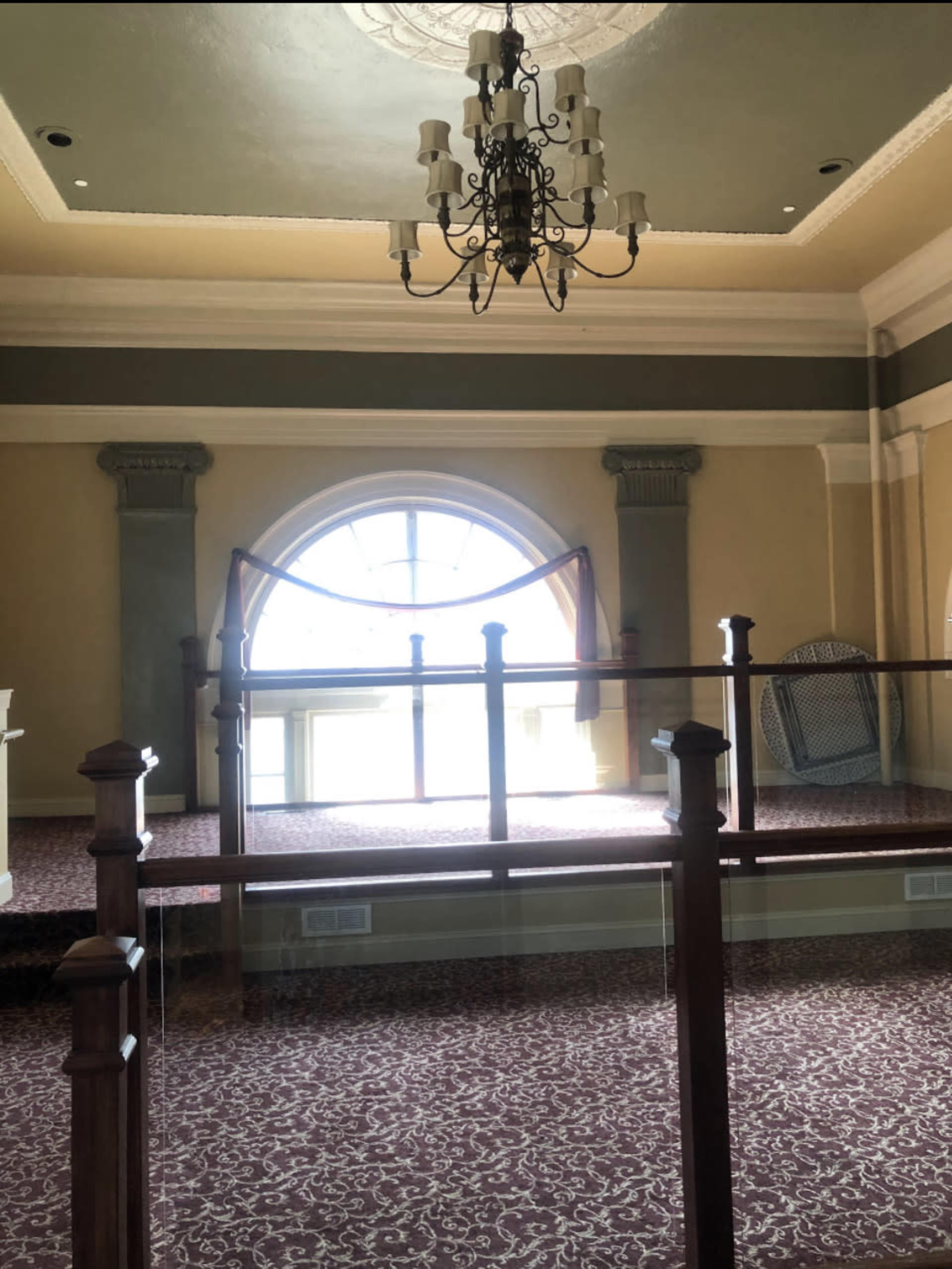 An elegant room with a large arched window, featuring a chandelier and decorative wall elements.