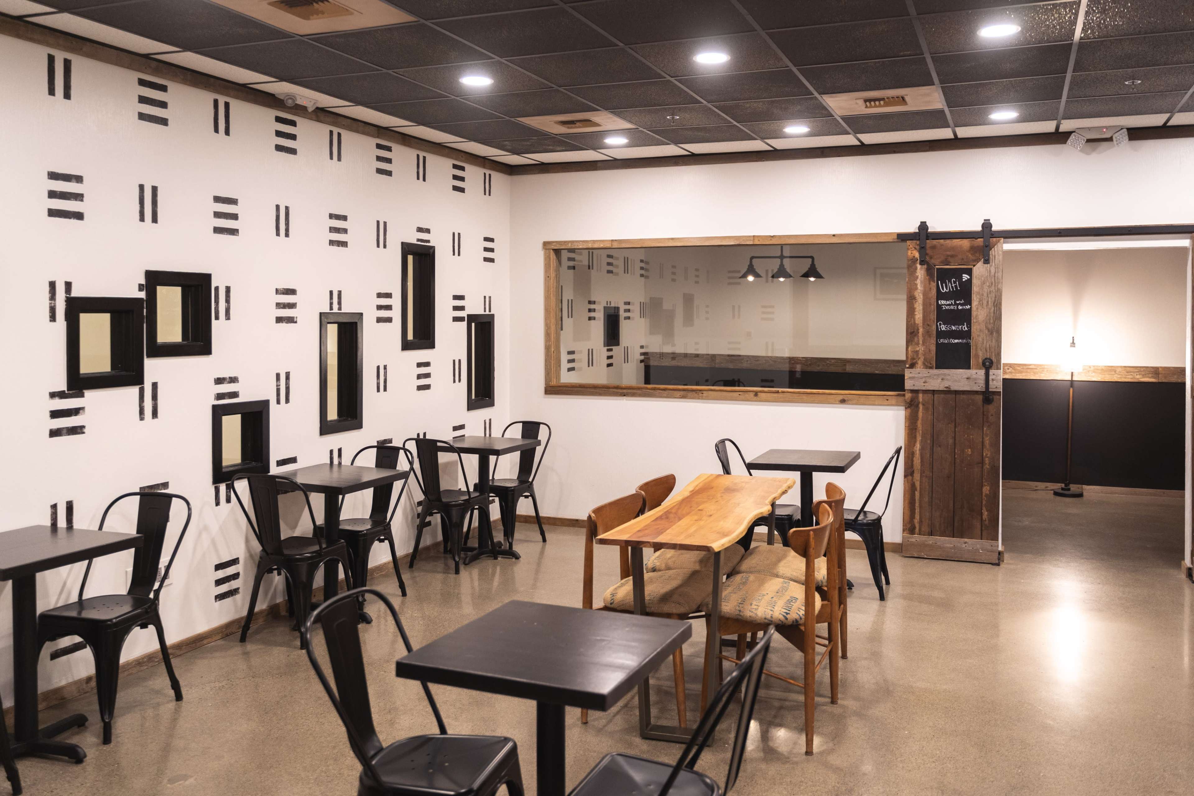 A minimalist cafe interior with black tables, wooden seating, and patterned walls.