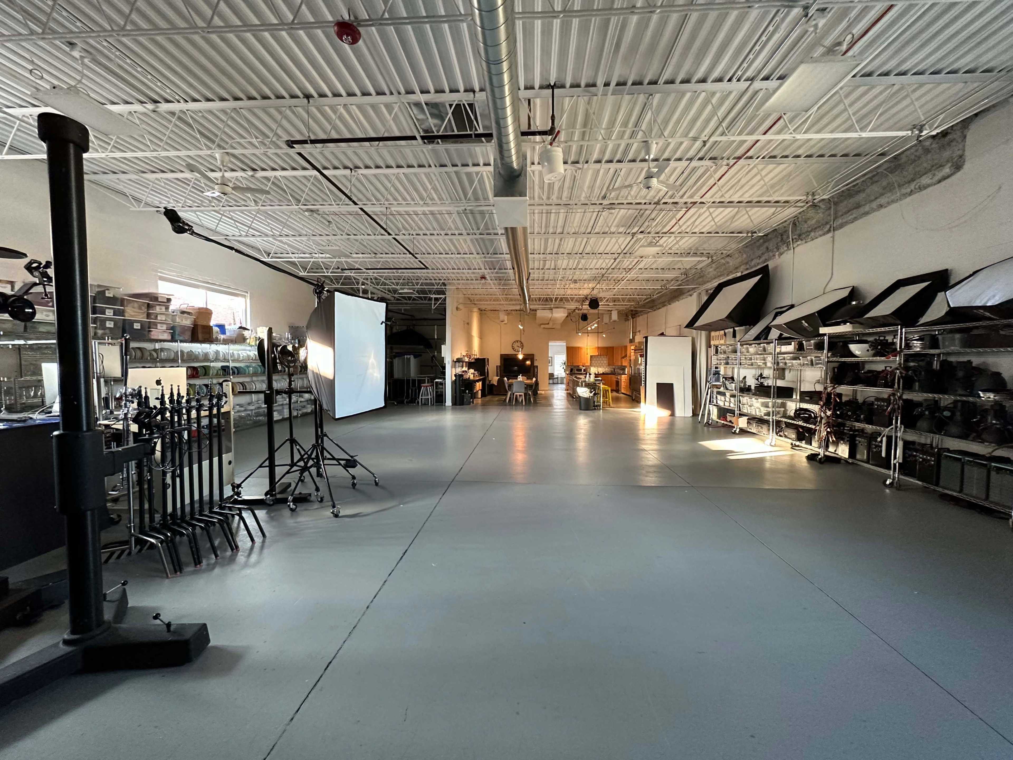 An empty studio space with various lighting equipment and shelves along the walls, filled with photography gear.
