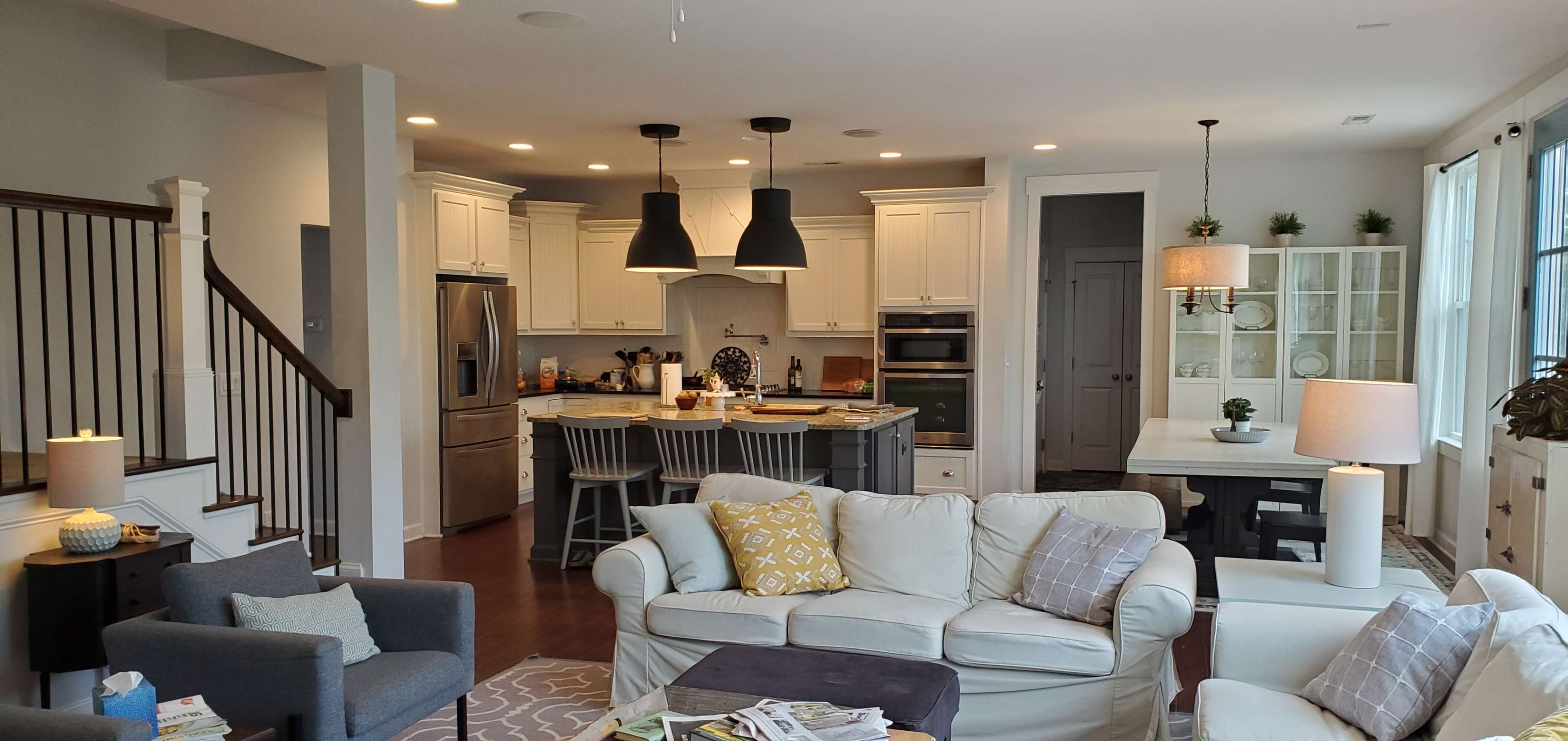 The image shows a modern, open-concept living space that includes a kitchen, dining area, and a cozy seating arrangement with light-colored furniture.
