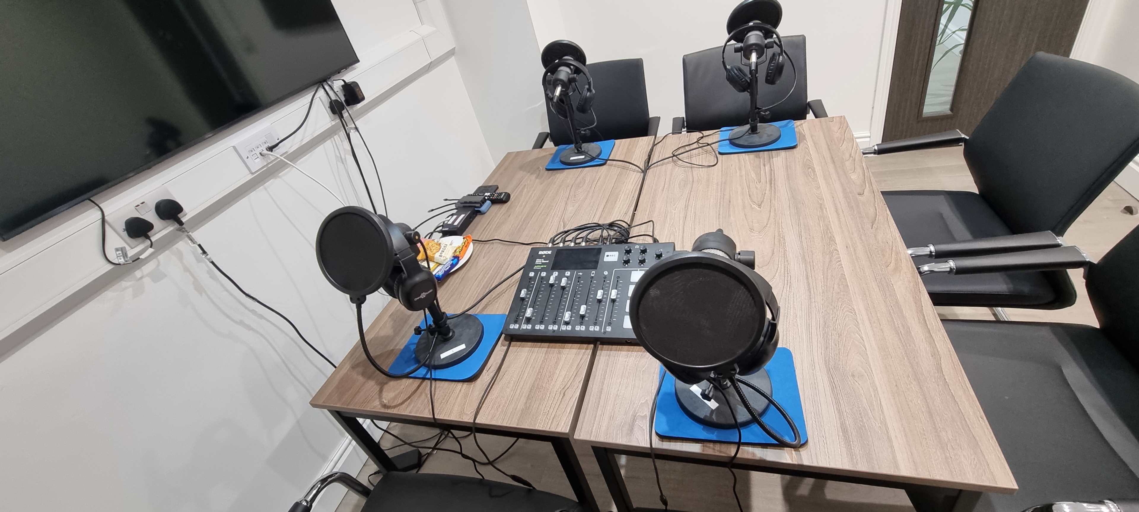 A table with four microphones and headsets is set up alongside a sound mixer in a recording studio.