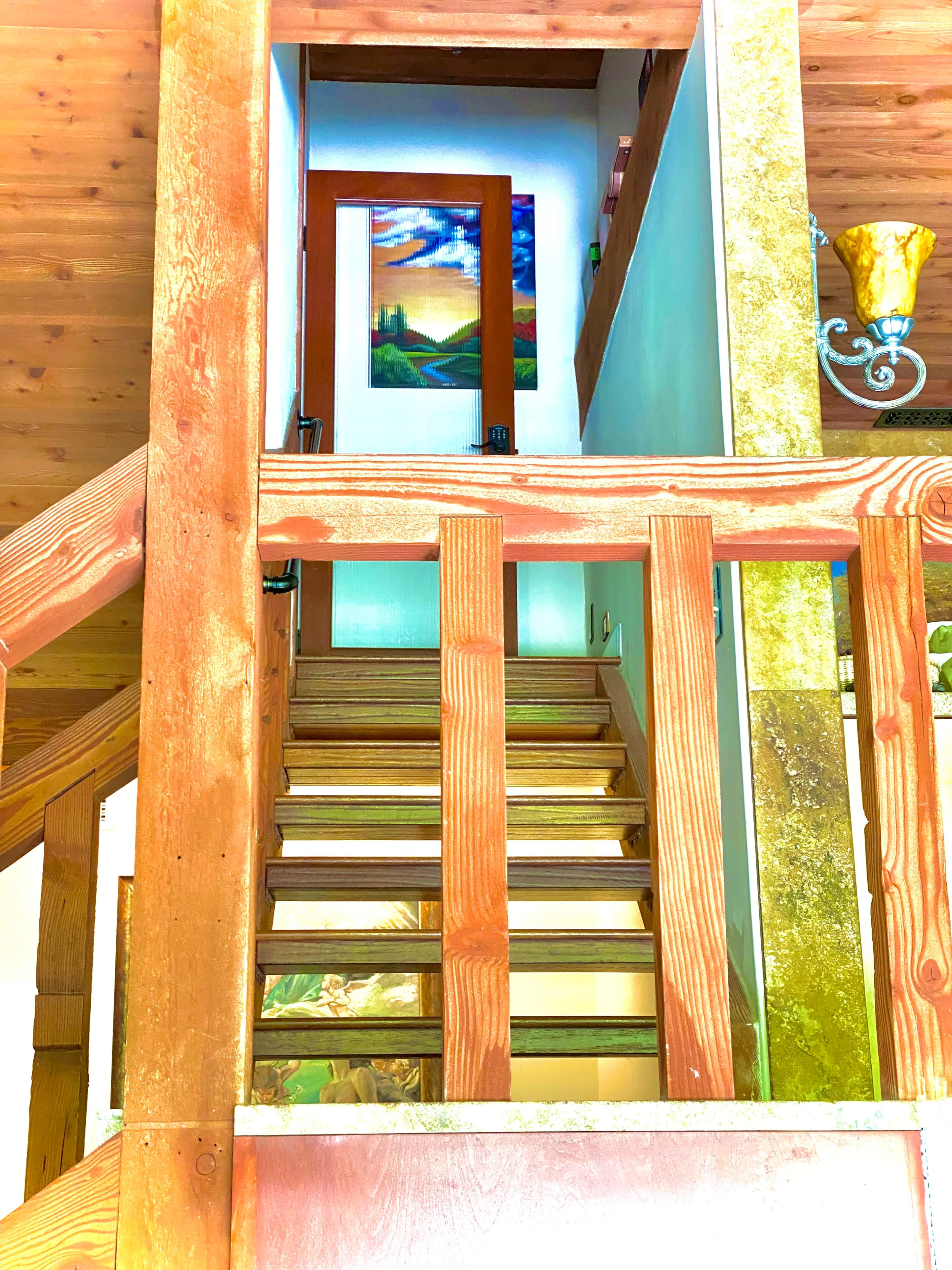 A wooden staircase leads to an upper level with a door and a painting visible in the background.