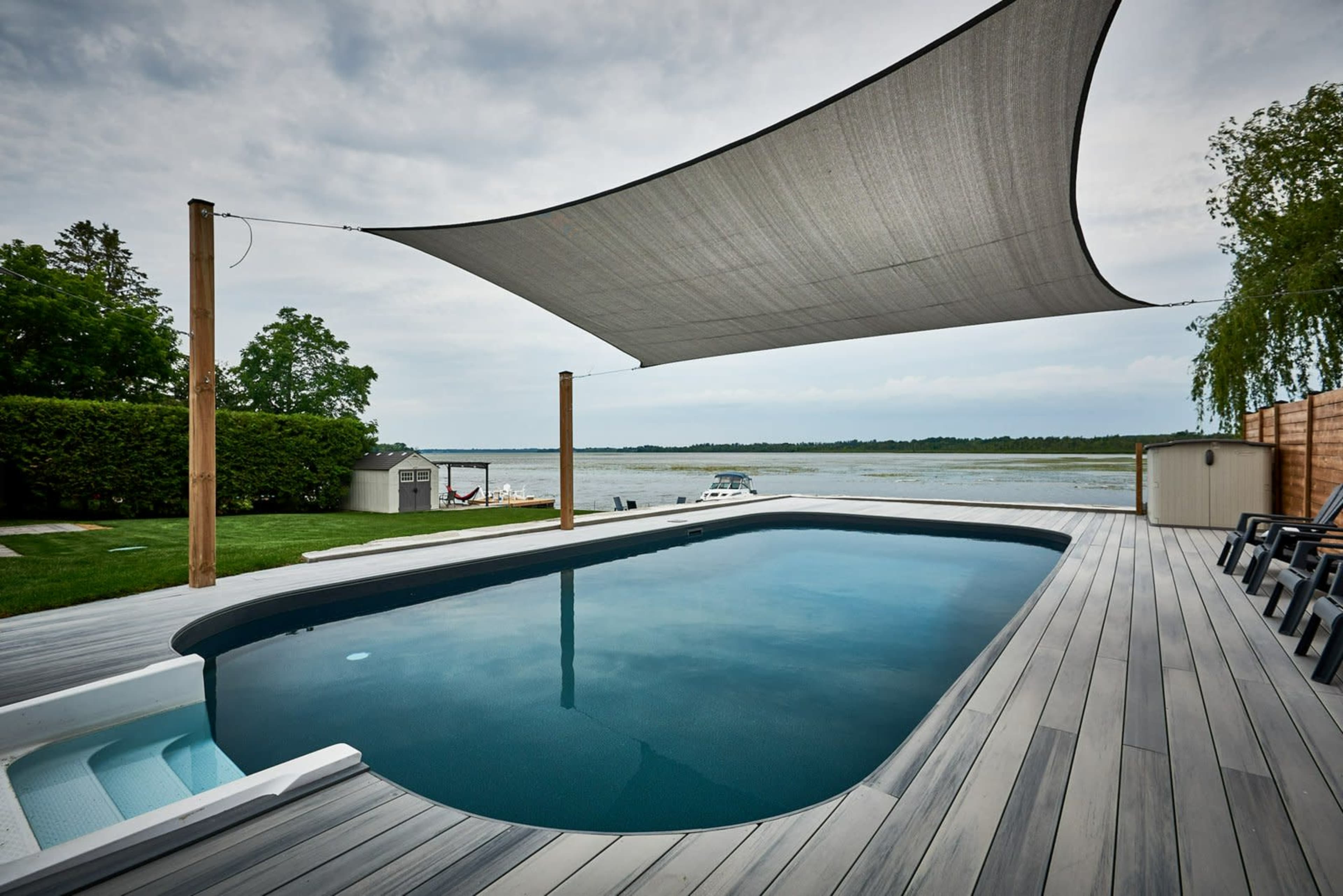 A rectangular swimming pool with a shaded area is set against a backdrop of a river and green landscape.